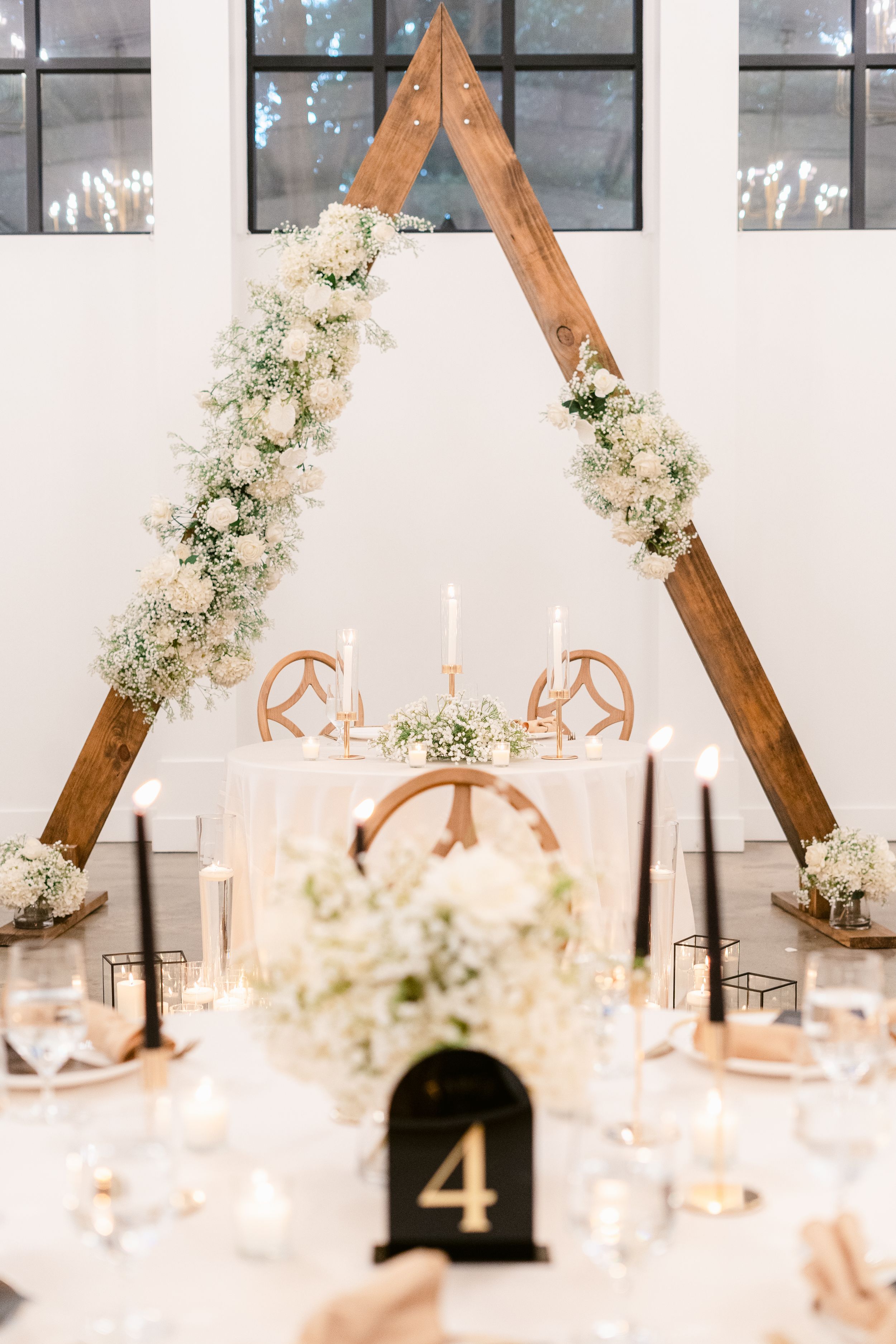 Elegant wedding table setting with wooden triangle arch decorated with white flowers and a table number 4 centerpiece.