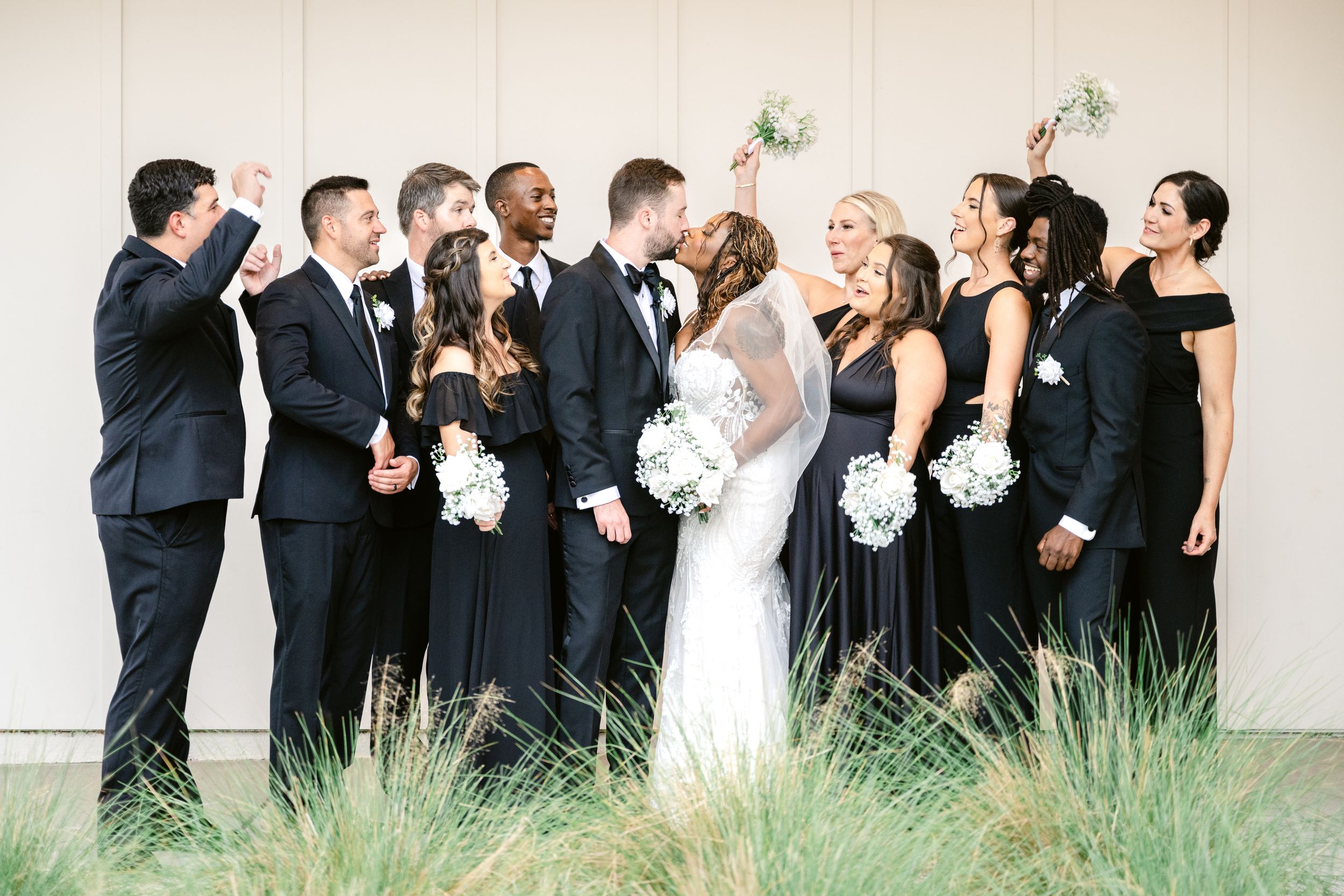Wedding party stands in line outdoors laughing and looking up at something in the sky together.
