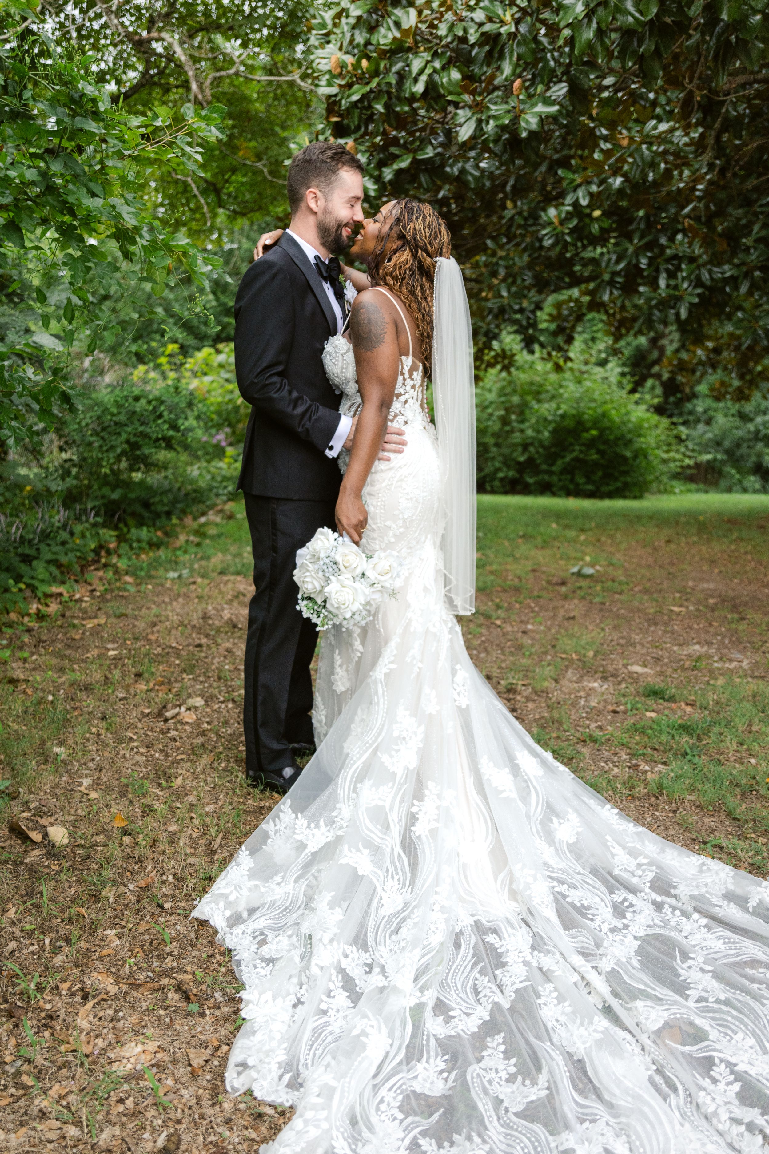 A romantic wedding portrait showing the dramatic sweep of a lace wedding gown train in a garden setting.