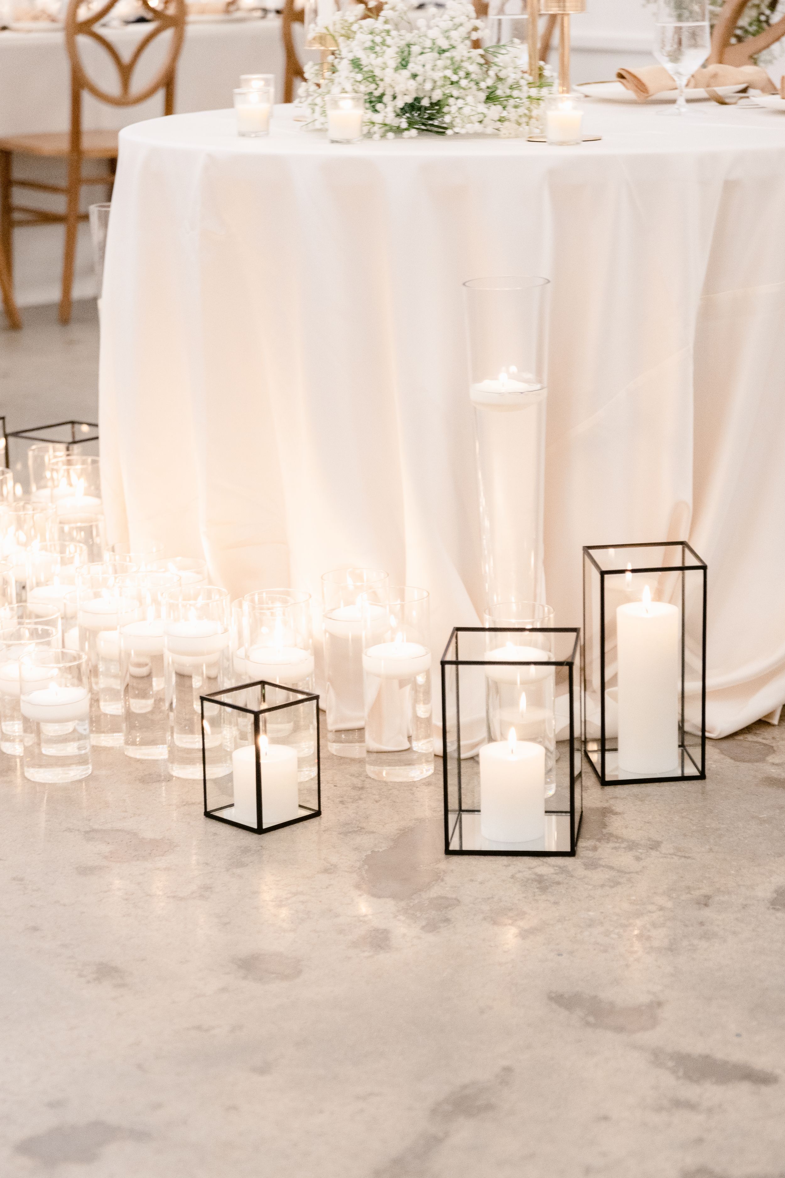 Modern wedding decor featuring black geometric lanterns and candles on a concrete floor.