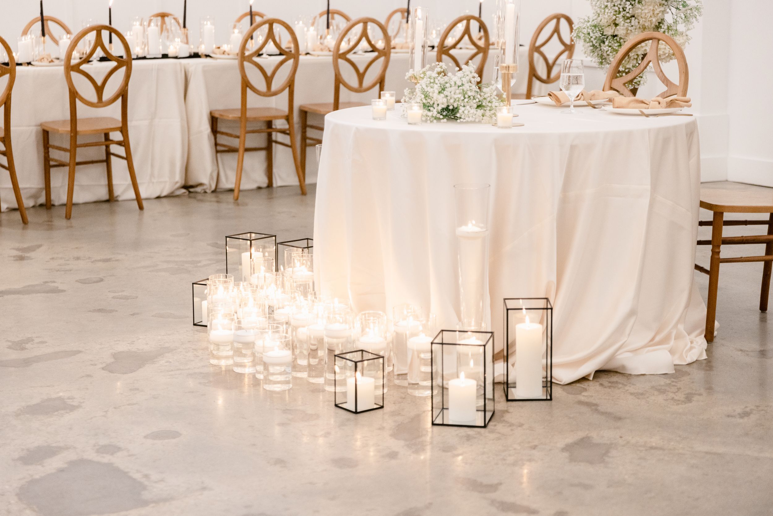 White lanterns with glowing candles line the aisle at an elegant indoor wedding ceremony setup.