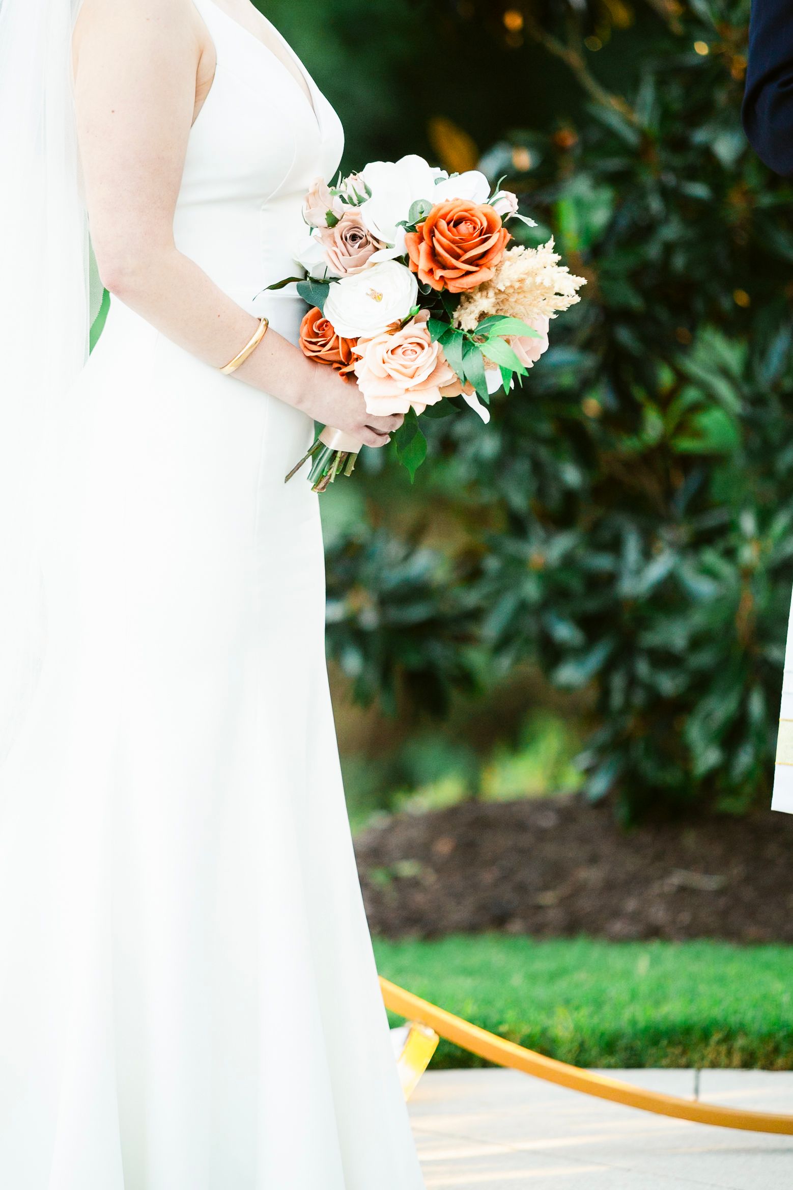Wedding bouquet with peach and coral roses held against a white bridal gown outdoors.