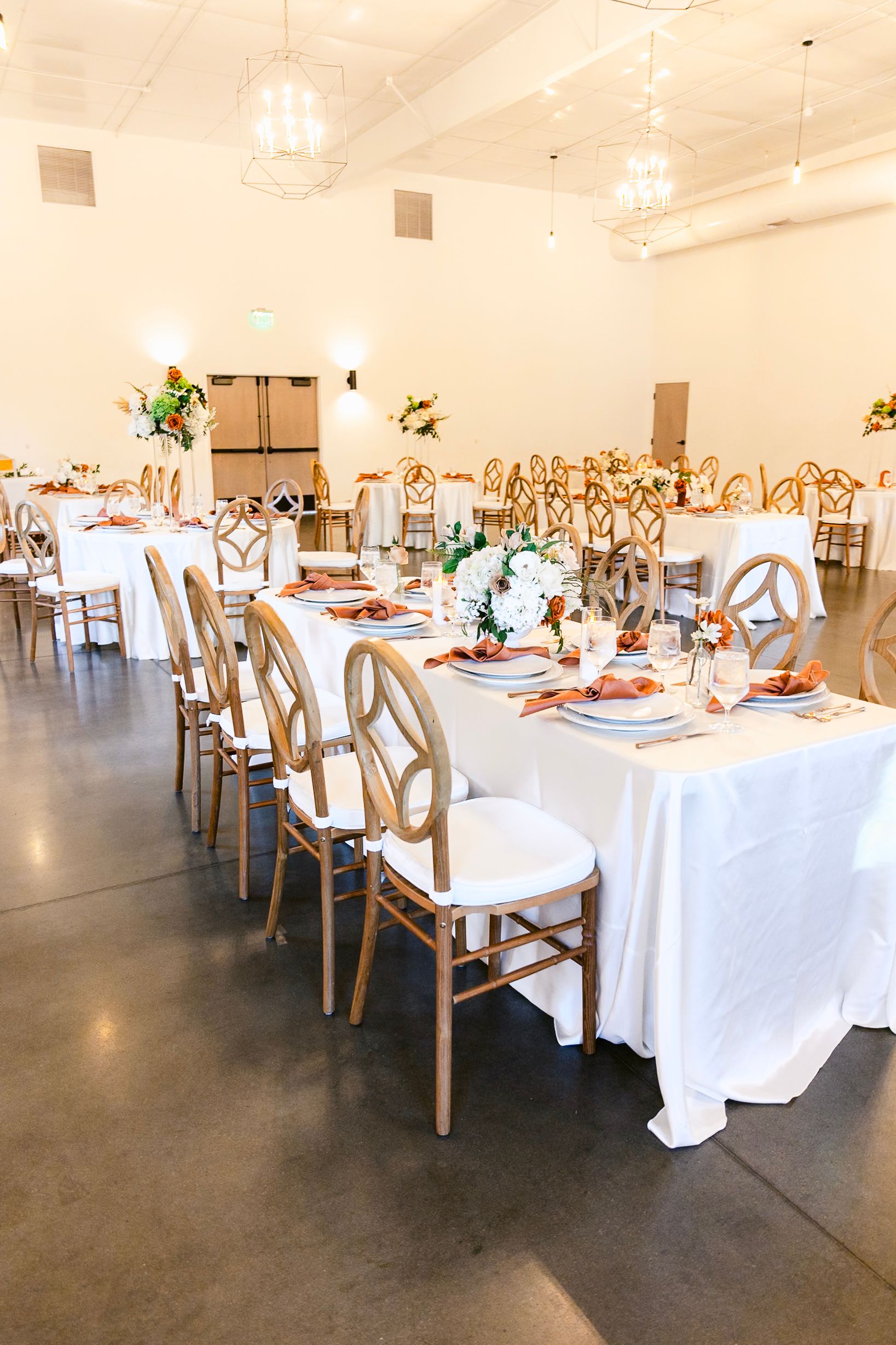 An elegant wedding reception venue with white tablecloths and wooden chairs set for a celebration.