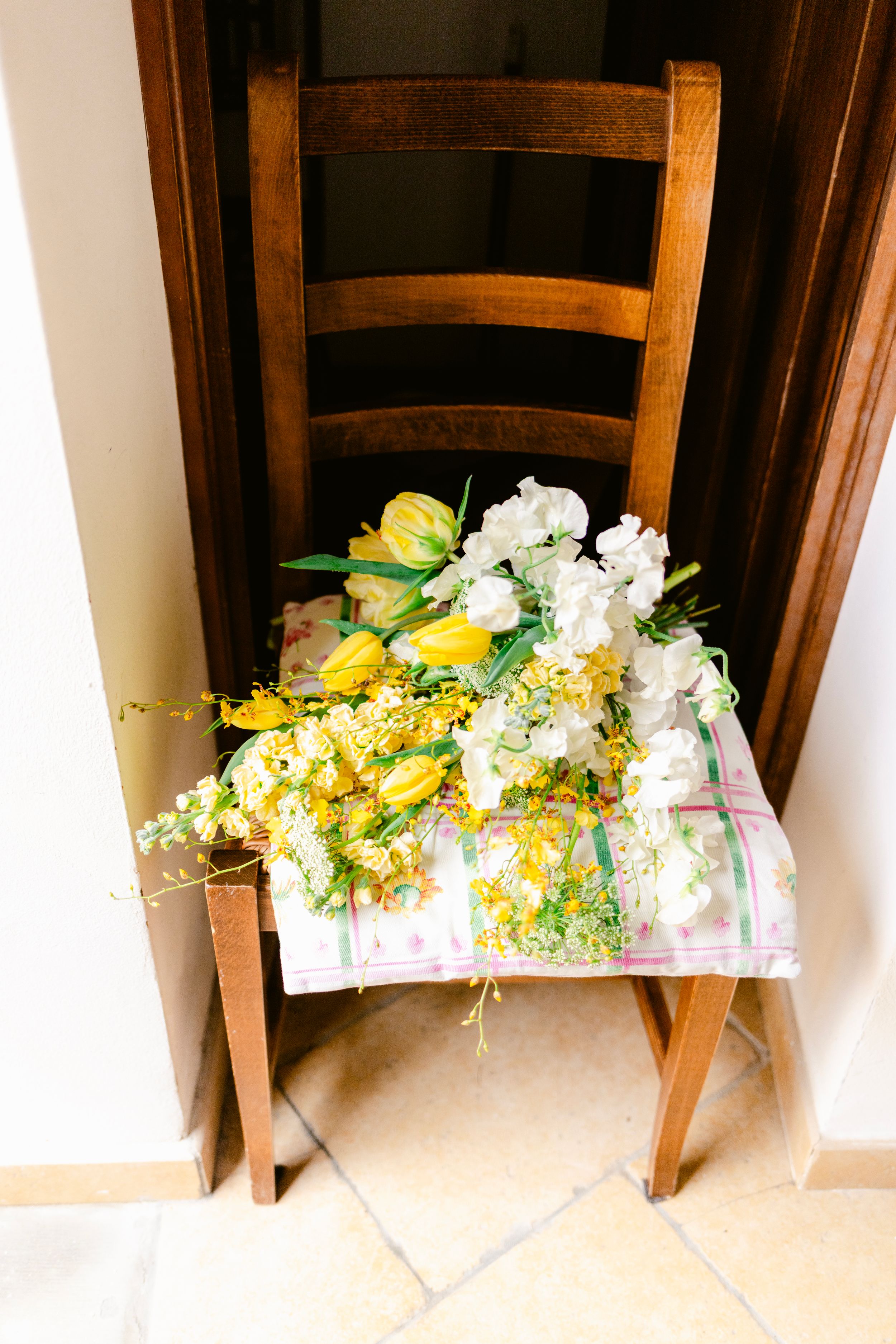 A rustic wooden chair adorned with a beautiful bouquet of yellow tulips and white flowers on a floral patterned cloth.