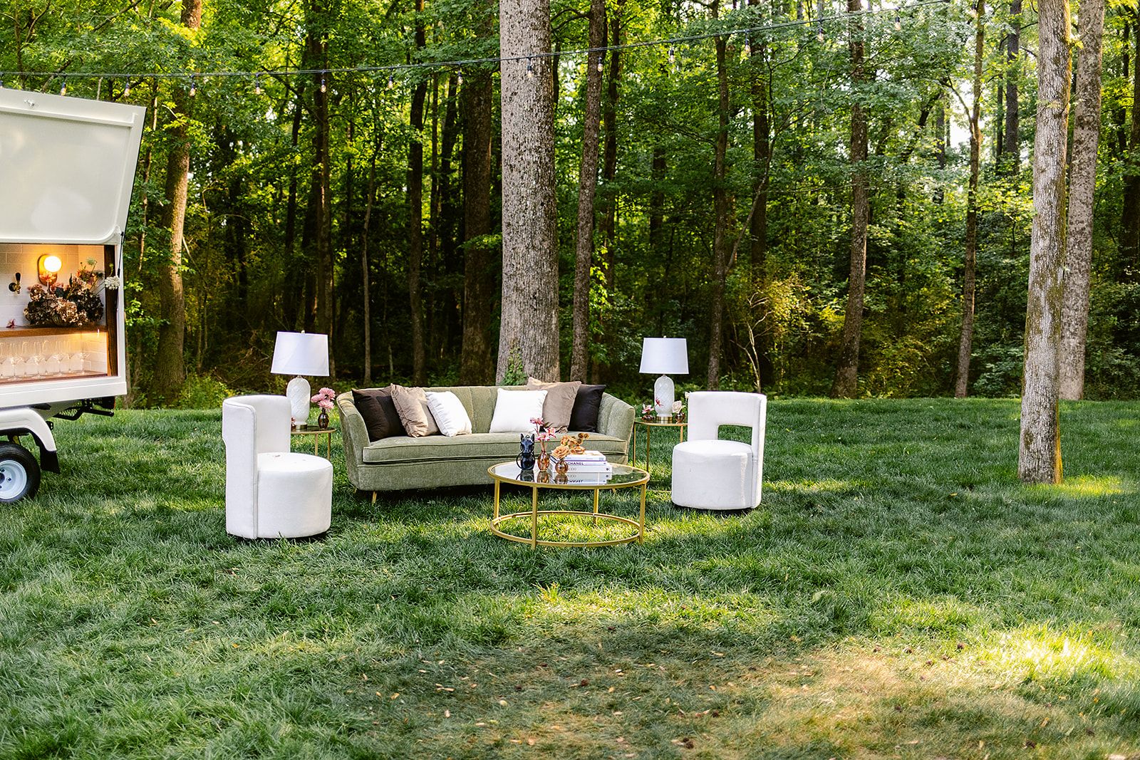 Outdoor wedding ceremony setup in a forest with white chairs and wooden arch decorated with flowers and greenery.