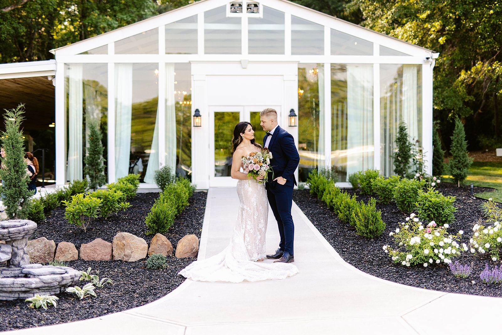 White greenhouse wedding venue with glass panels and landscaped gardens in golden sunlight.