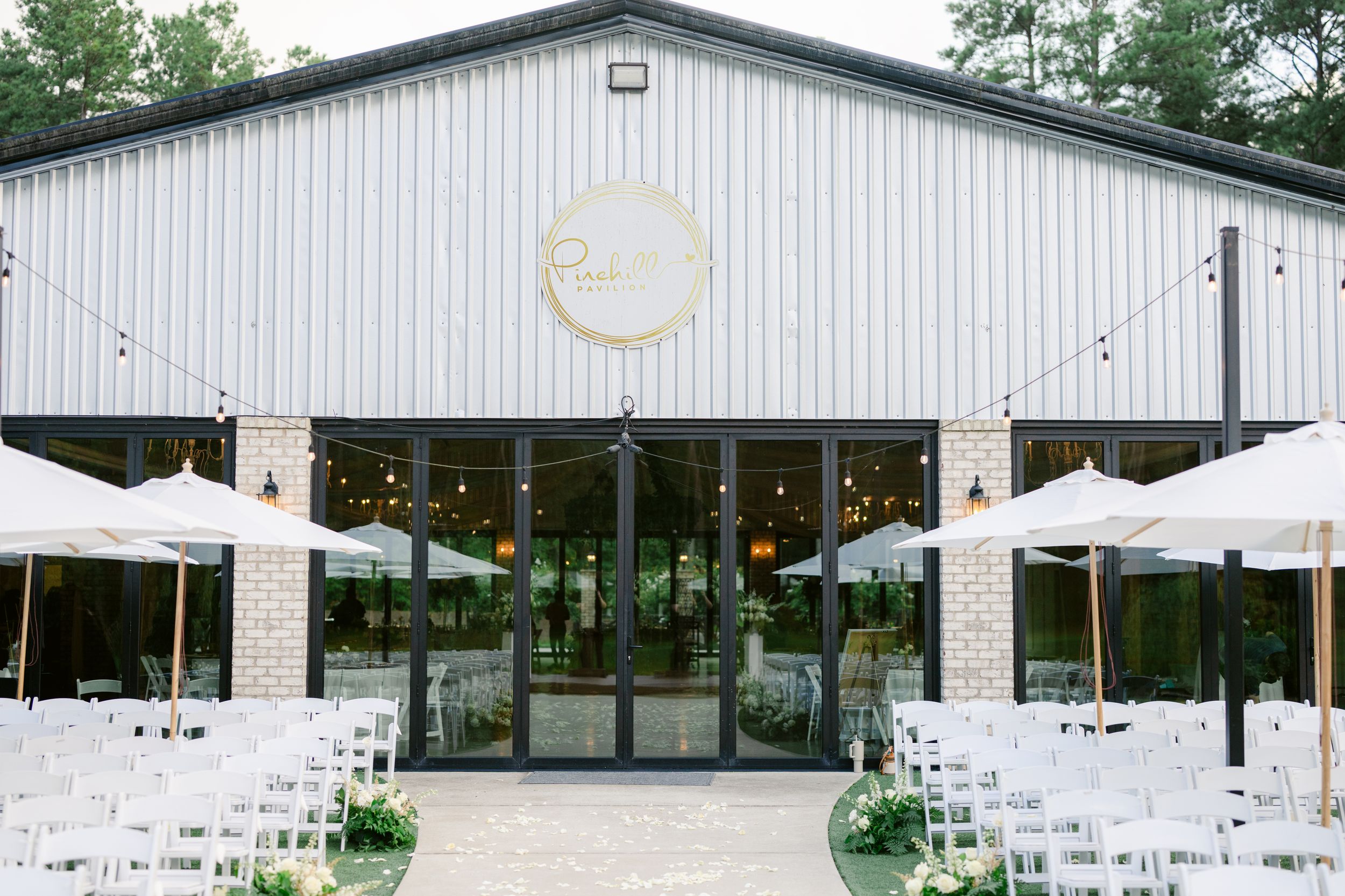Modern white pavilion with outdoor seating arranged for a wedding reception under a forest canopy.