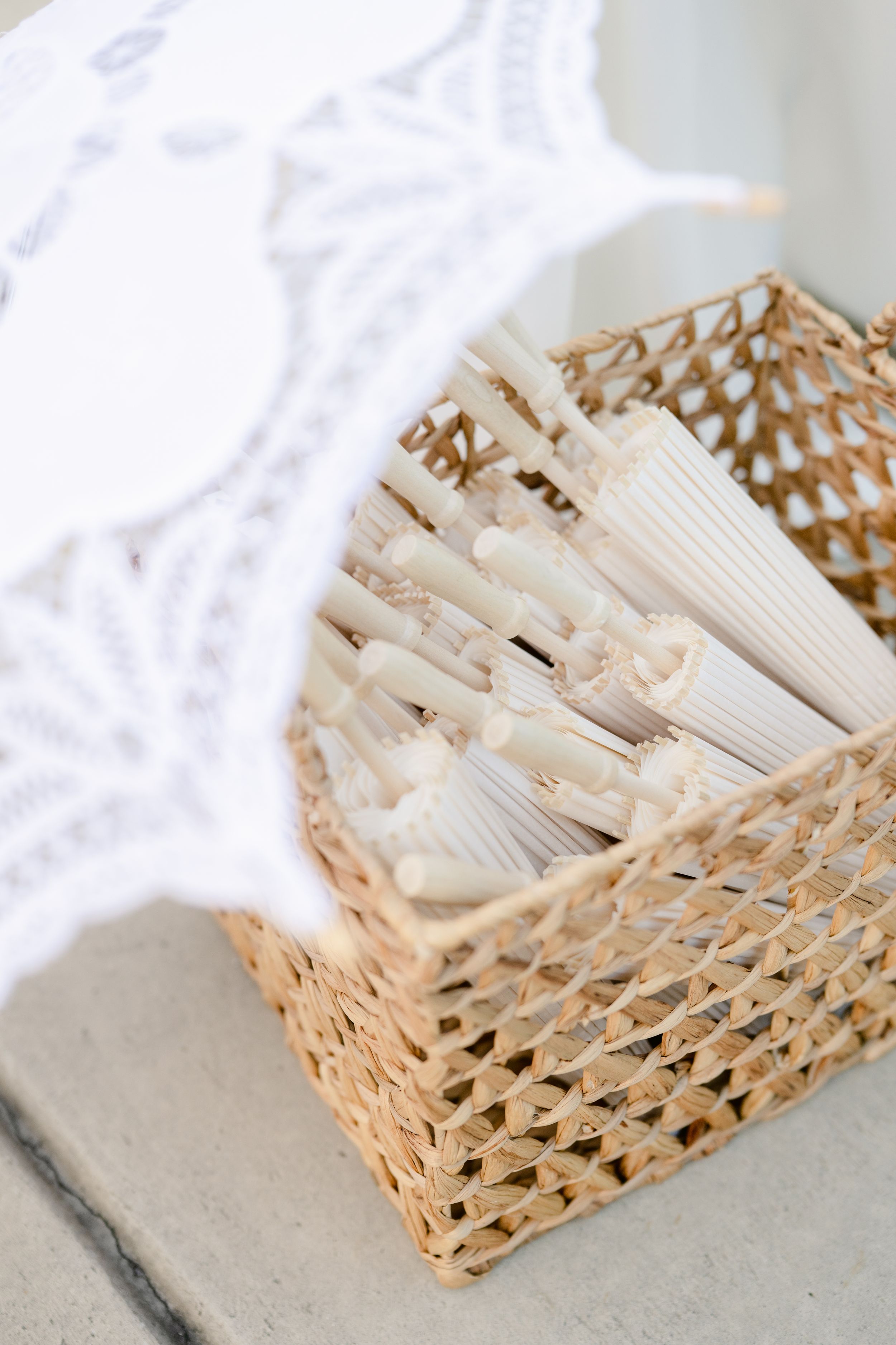 Woven bamboo basket filled with white paper napkins arranged neatly on a light gray surface.