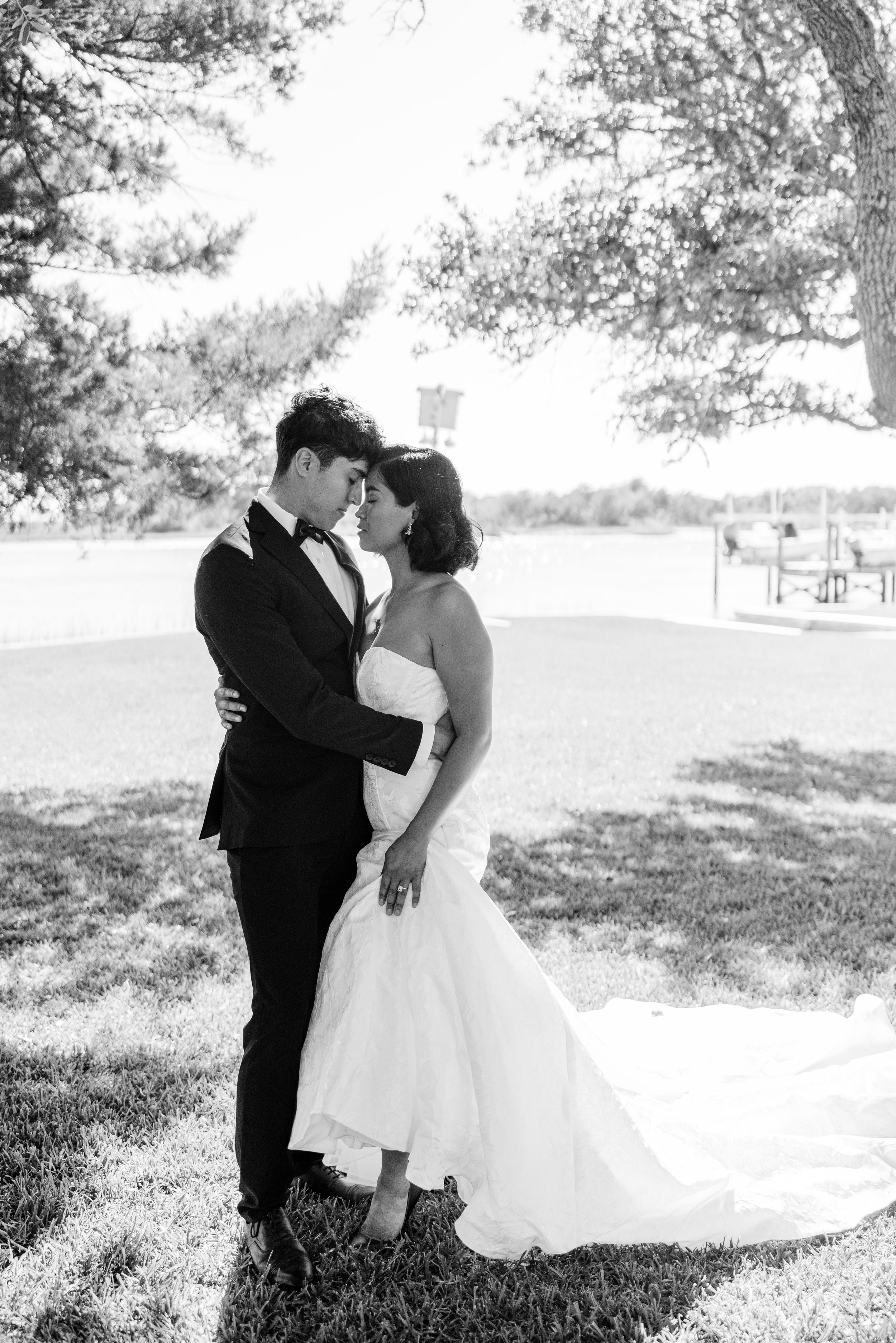 A romantic black and white wedding photo capturing a tender moment between newlyweds outdoors.