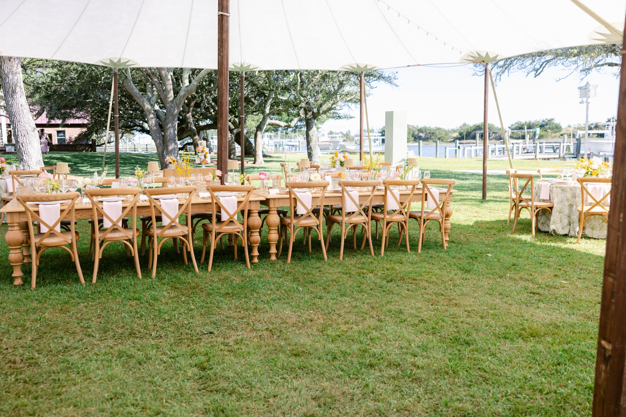 White wedding tents and wooden chairs arranged on a lush green lawn for an outdoor celebration.