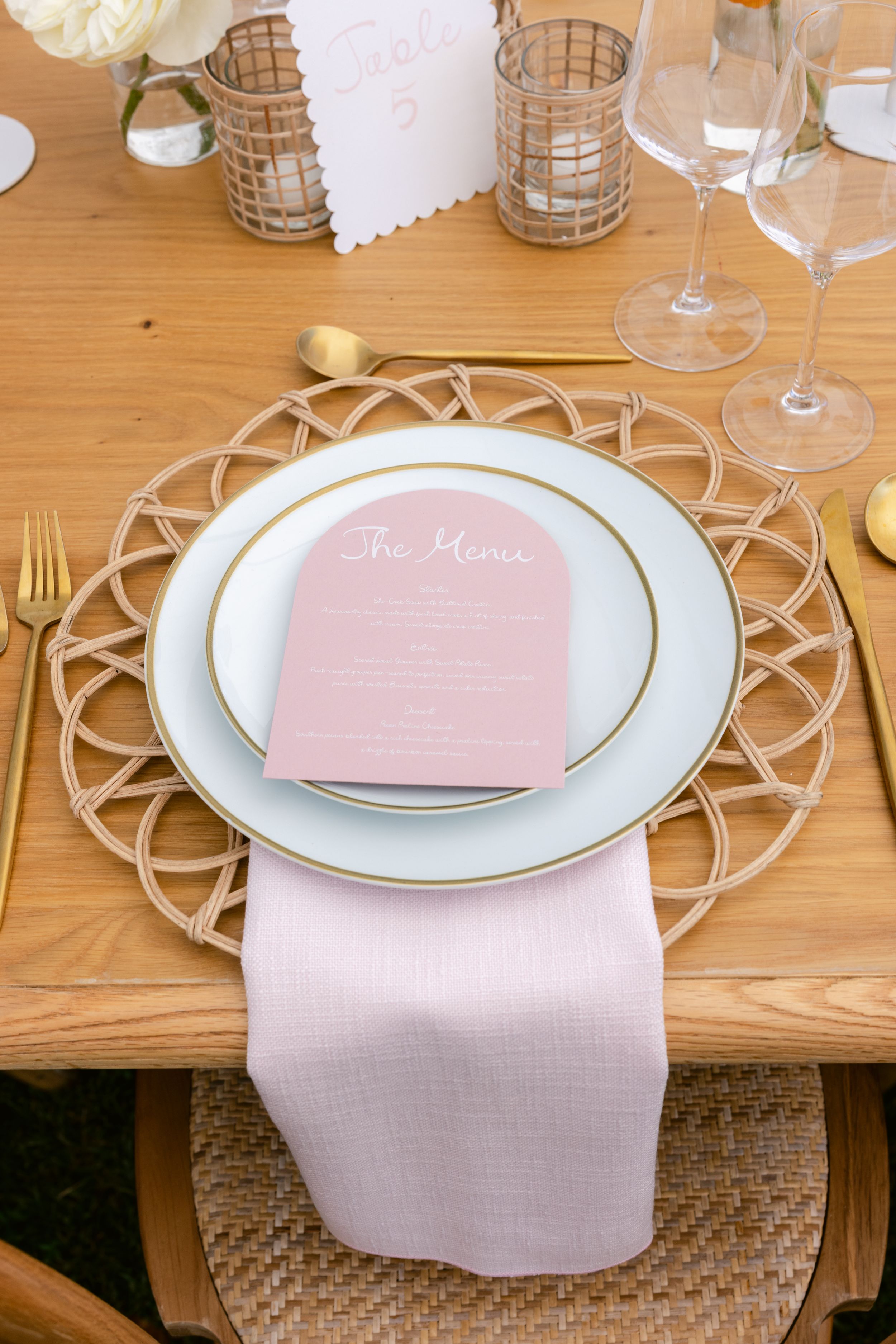 Elegant place setting with pink menu card on white plates with gold flatware and geometric charger.