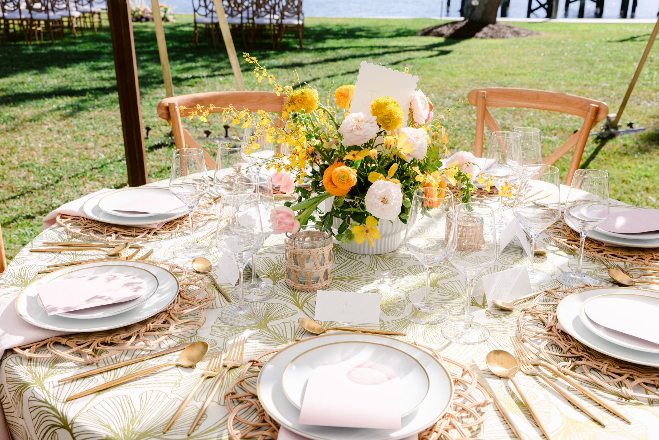 Elegant round table setting with yellow and white floral centerpiece and gold accents.