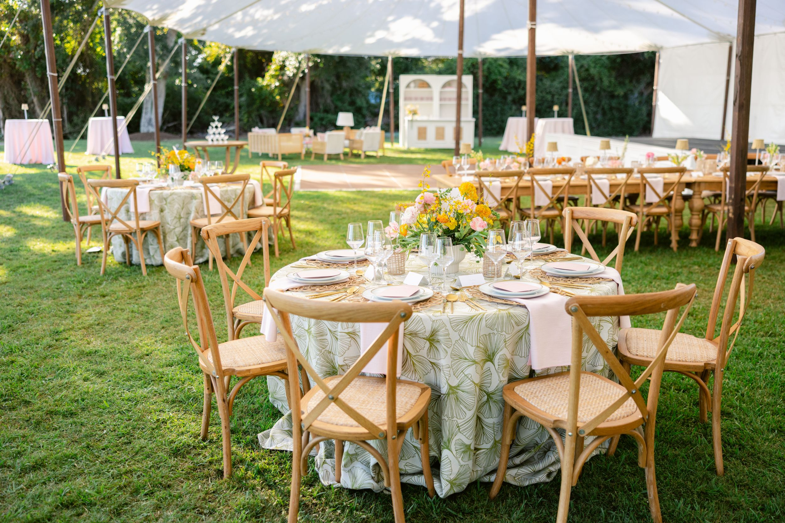 Outdoor wedding reception setup with wooden chairs and floral centerpieces under a white tent.
