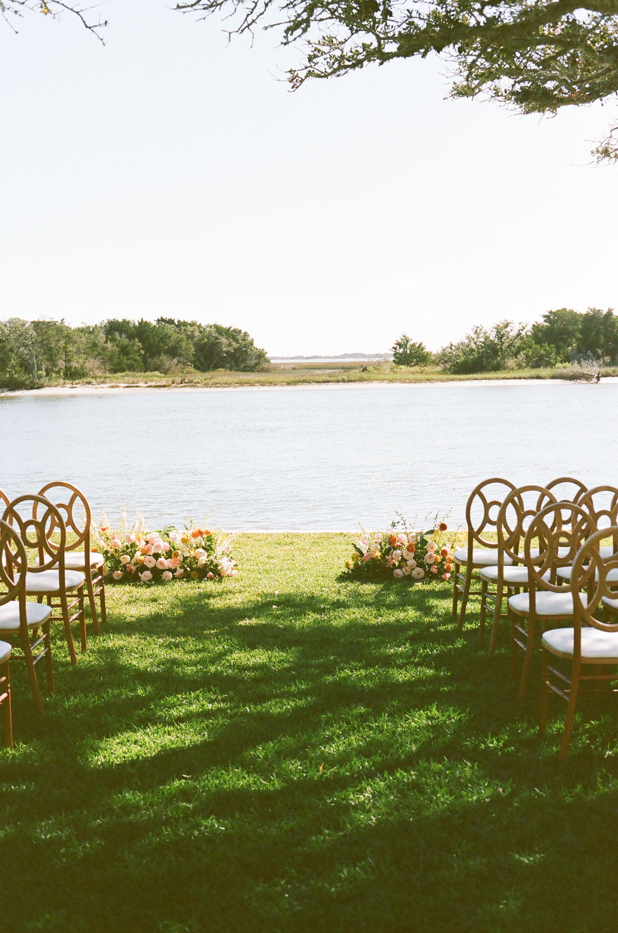 Rustic wooden cross-back chairs arranged for an outdoor waterfront wedding ceremony.