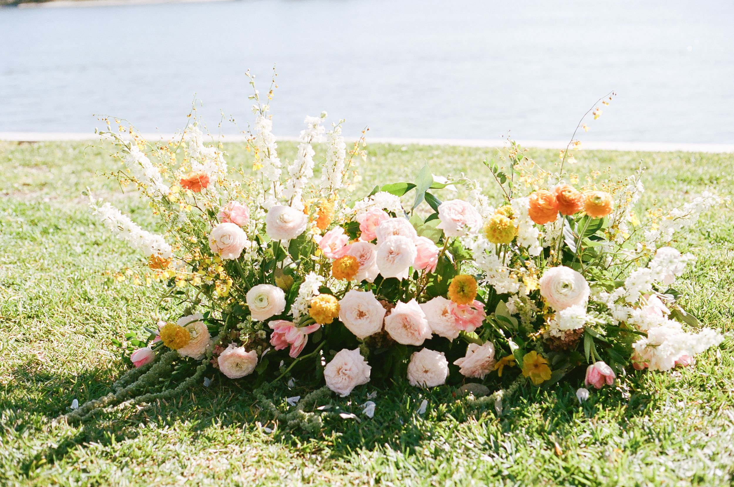Romantic peach and white floral arrangements line the ground creating a beautiful outdoor wedding aisle.