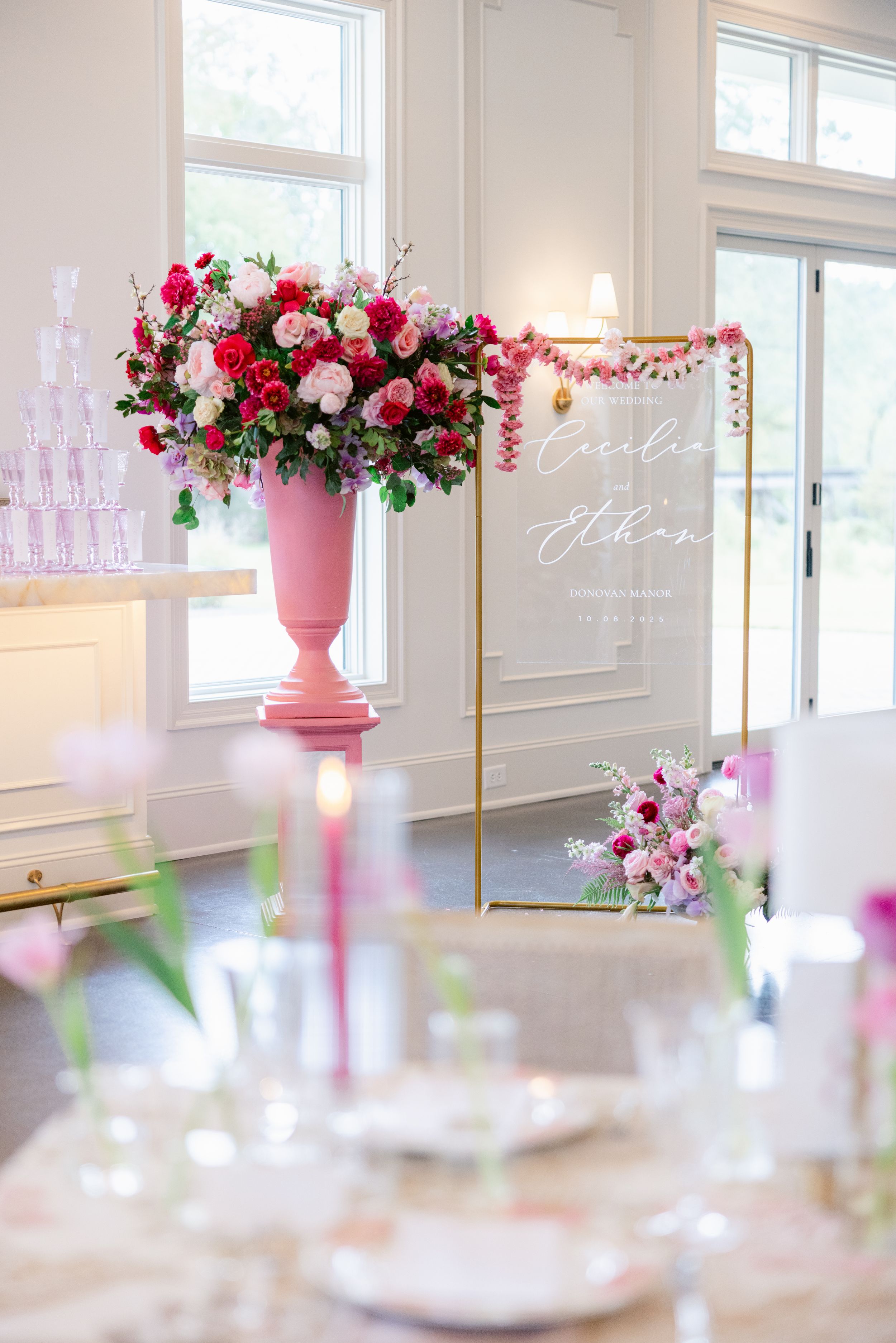 Elegant wedding reception table setup with pink floral centerpieces and soft lighting in a bright white room.