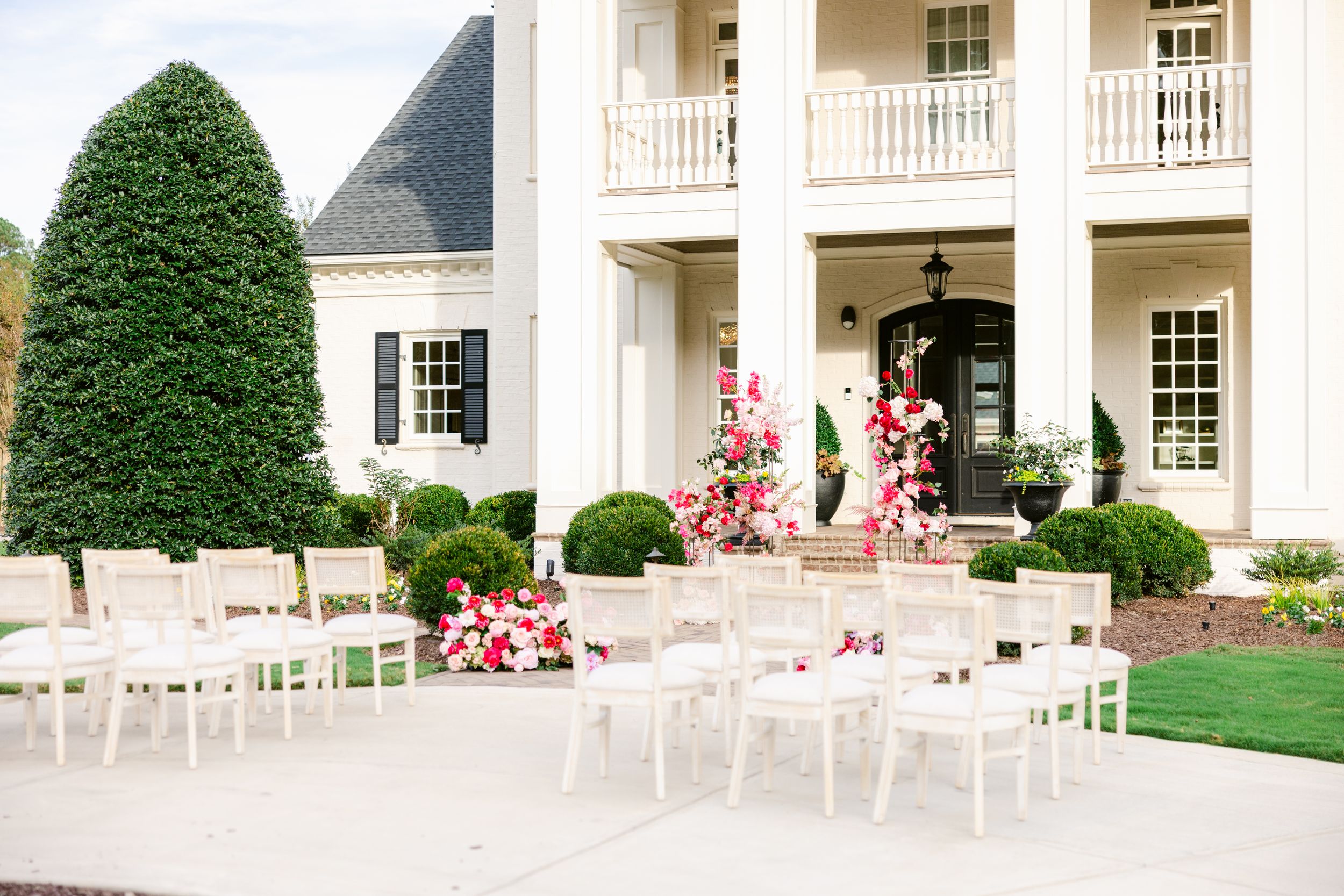 Classic white colonial-style wedding venue exterior with pink floral decorations and white chairs.