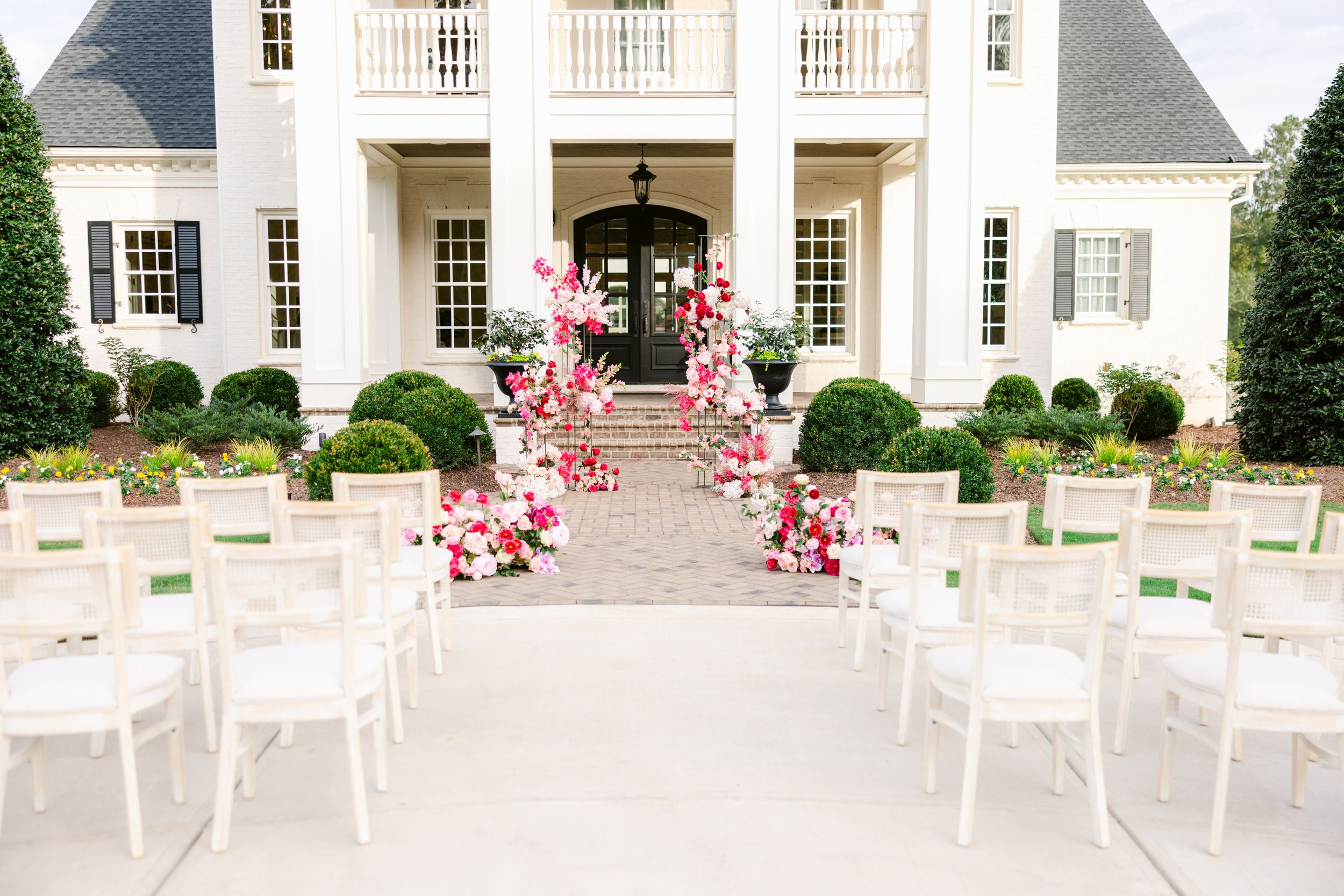 Elegant white colonial mansion exterior with manicured landscaping and ceremony seating.