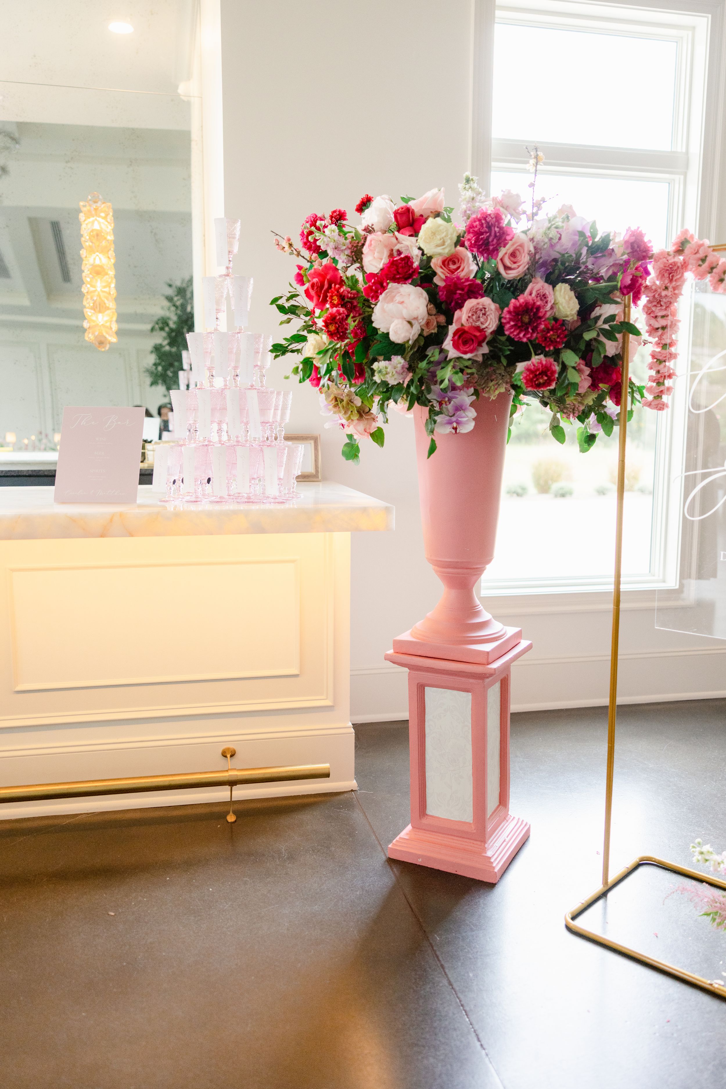 Pink pedestal vase with luxurious floral arrangement against white piano backdrop.