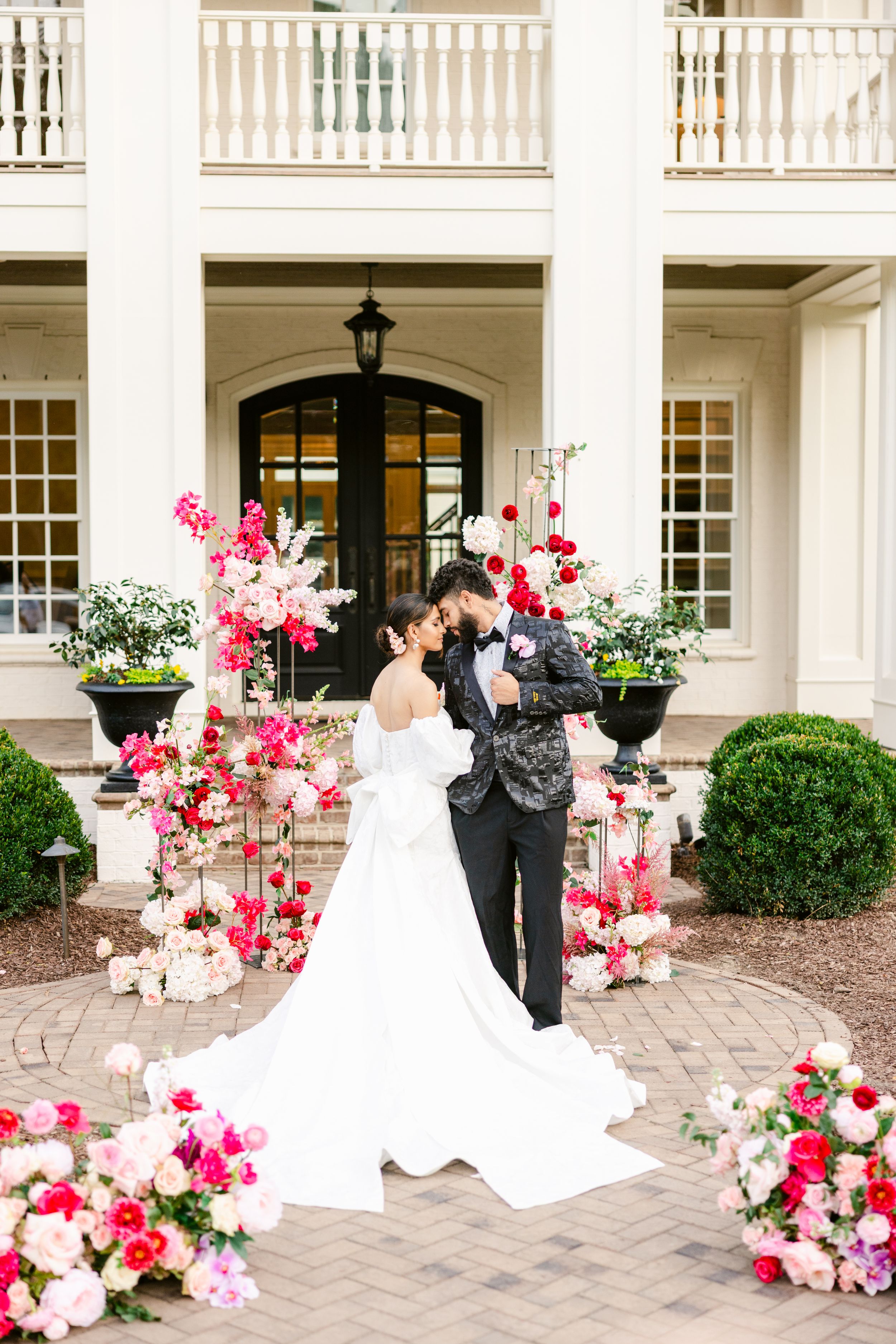 Wedding couple posing on brick patio with pink and red floral arrangements.