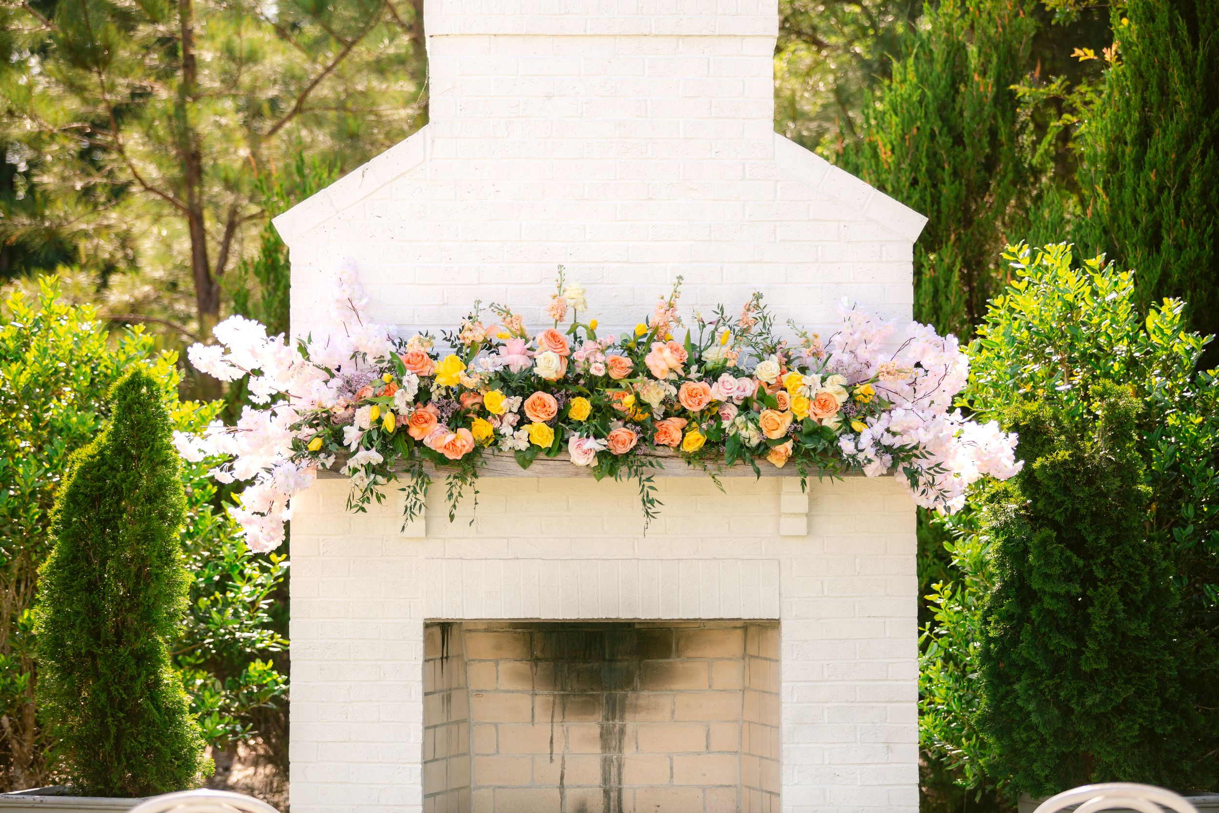 A white outdoor wedding gazebo decorated with colorful floral arrangements and greenery in a garden setting.