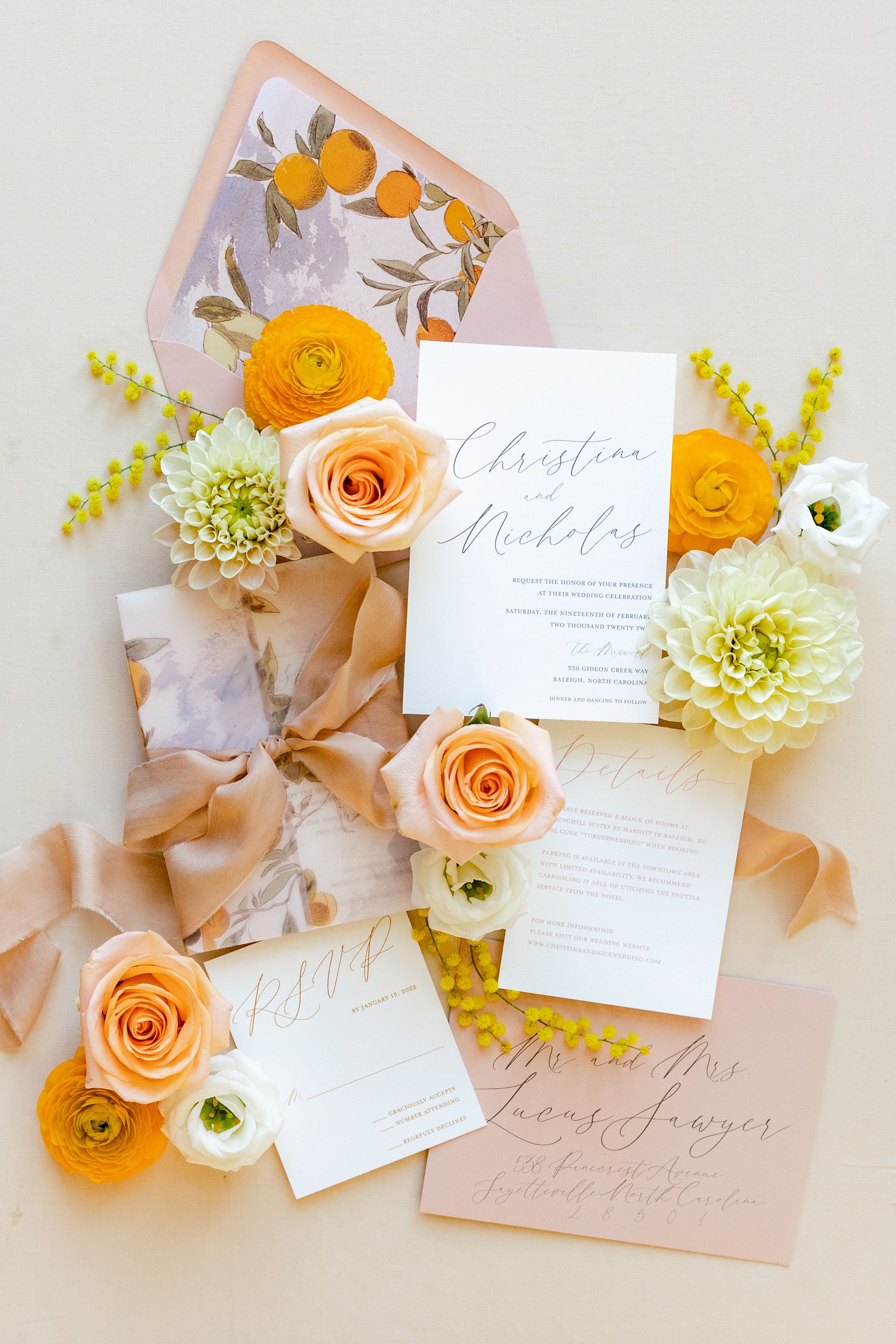 Wedding stationery with peach and orange roses, ranunculus flowers, and calligraphy on a light marble background.