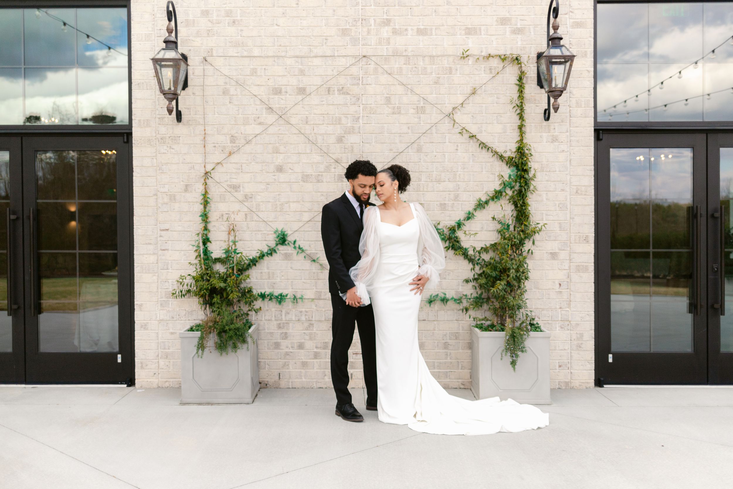 Wedding couple shares intimate moments against modern stone wall backdrop with greenery and black doors.
