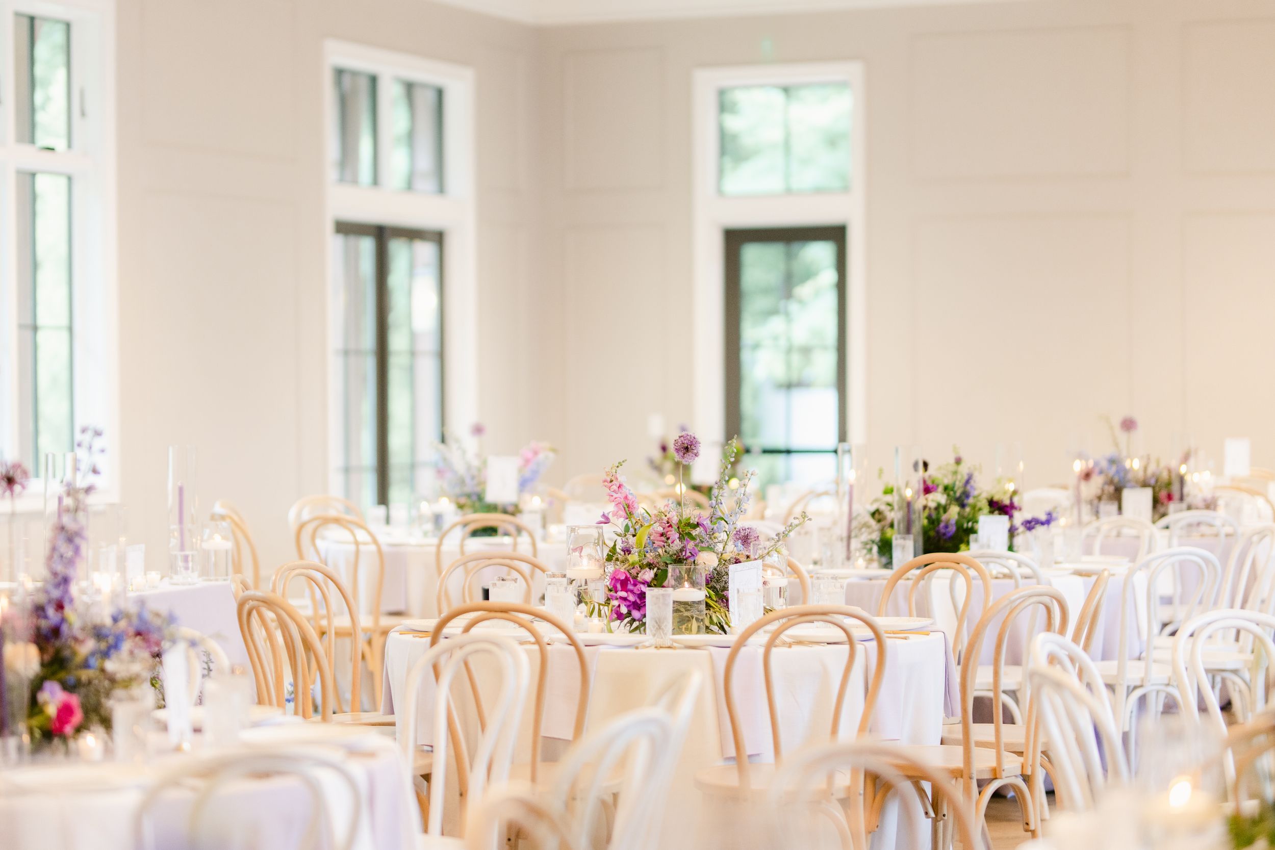 Elegant wedding reception venue with white bentwood chairs and pink floral centerpieces in natural light.