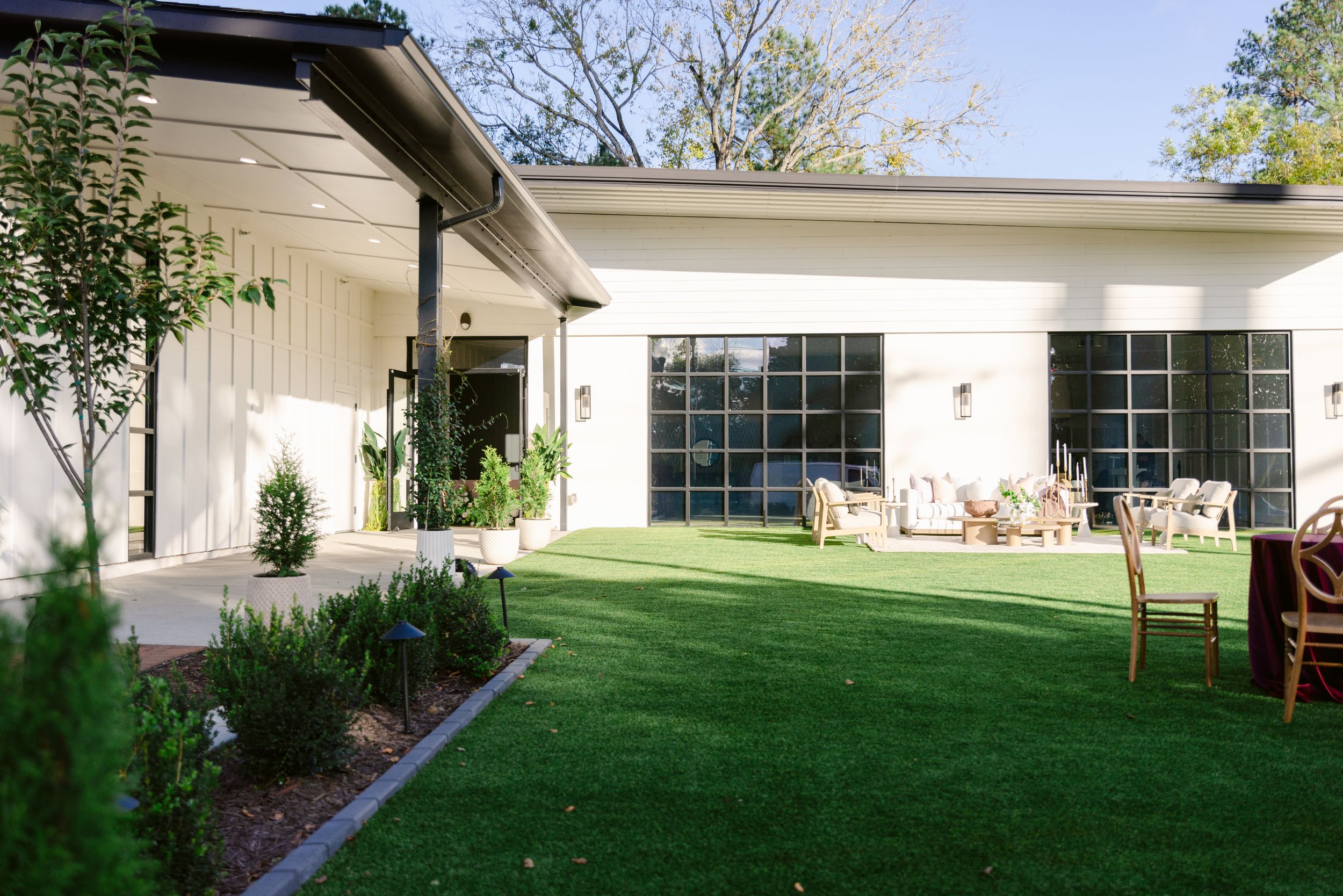 A panoramic view of a modern white house exterior with manicured lawn and landscaping in daylight.