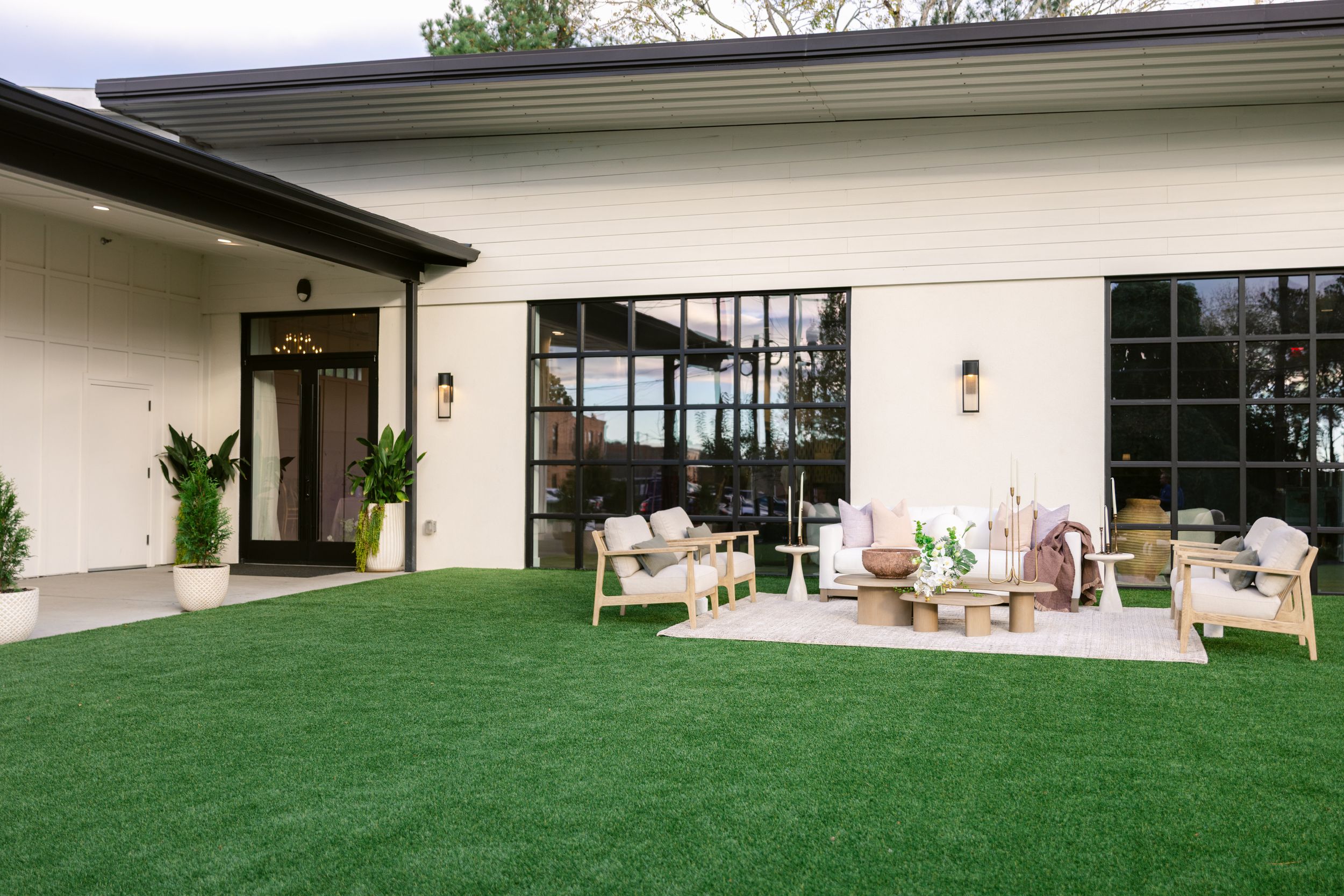 Modern white building exterior with floor-to-ceiling windows and green lawn landscaping creates a sleek architectural design.