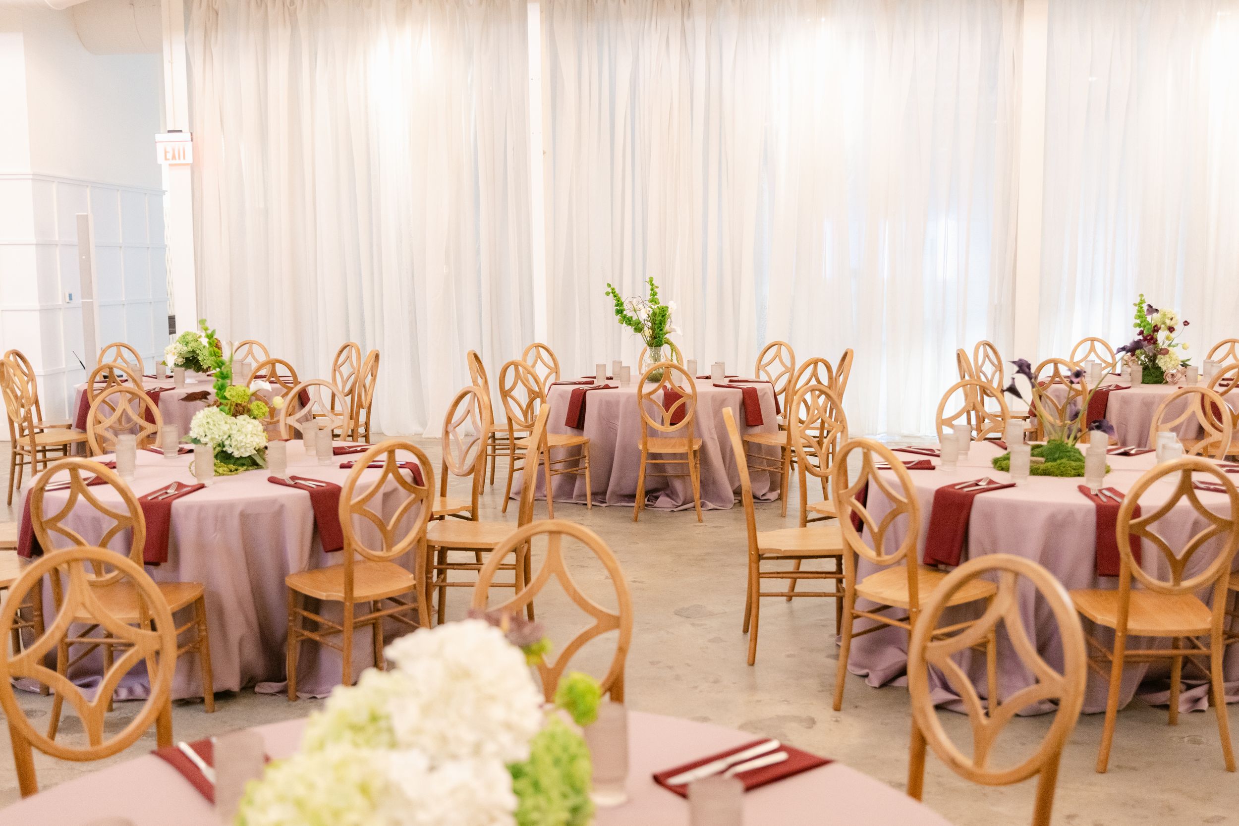 Elegant wedding reception venue with wooden chairs and white drapes creating a romantic, ethereal atmosphere.