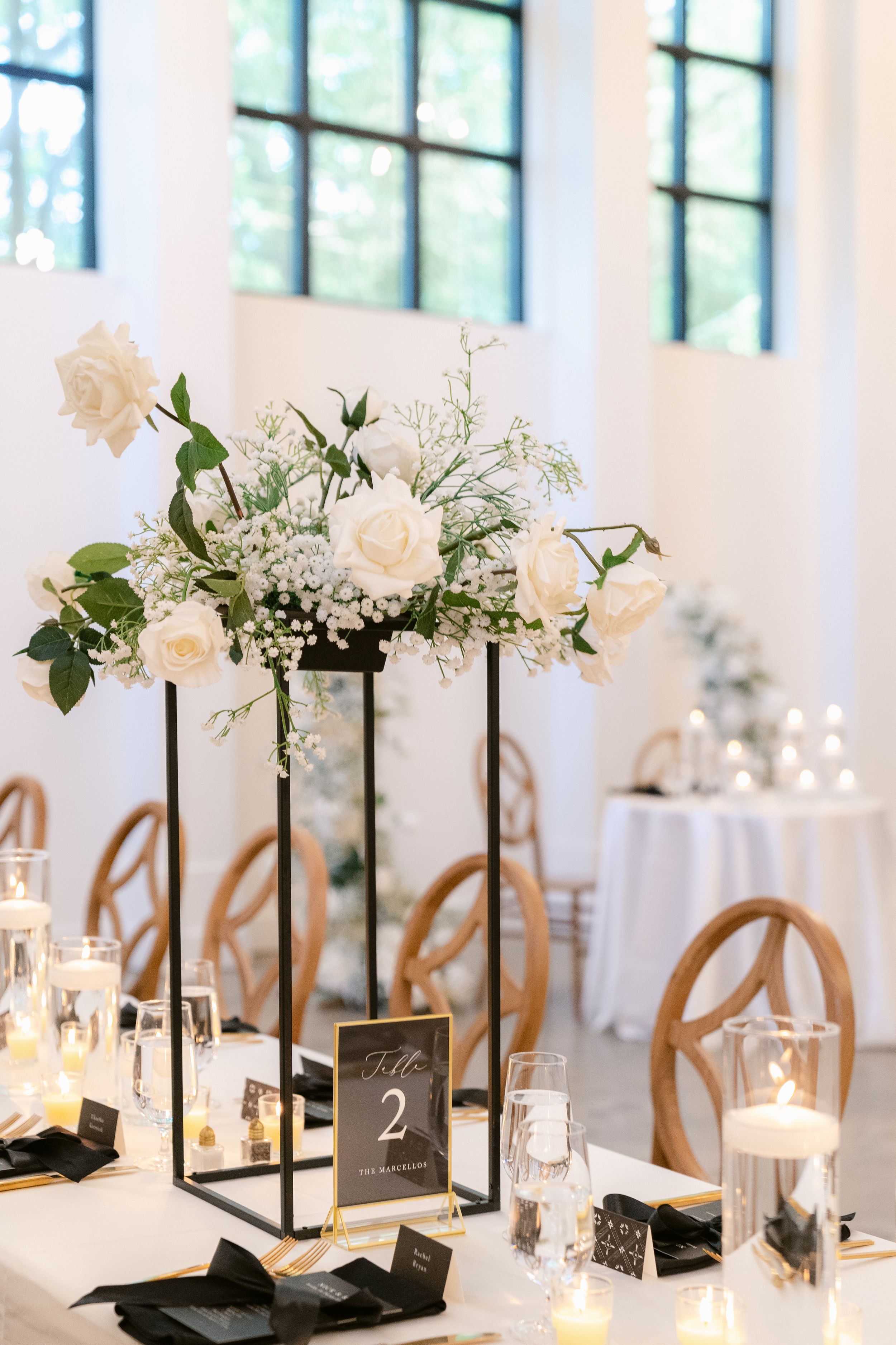 Elegant wedding reception table decor with white lanterns, floral arrangements and table numbers in black frames.
