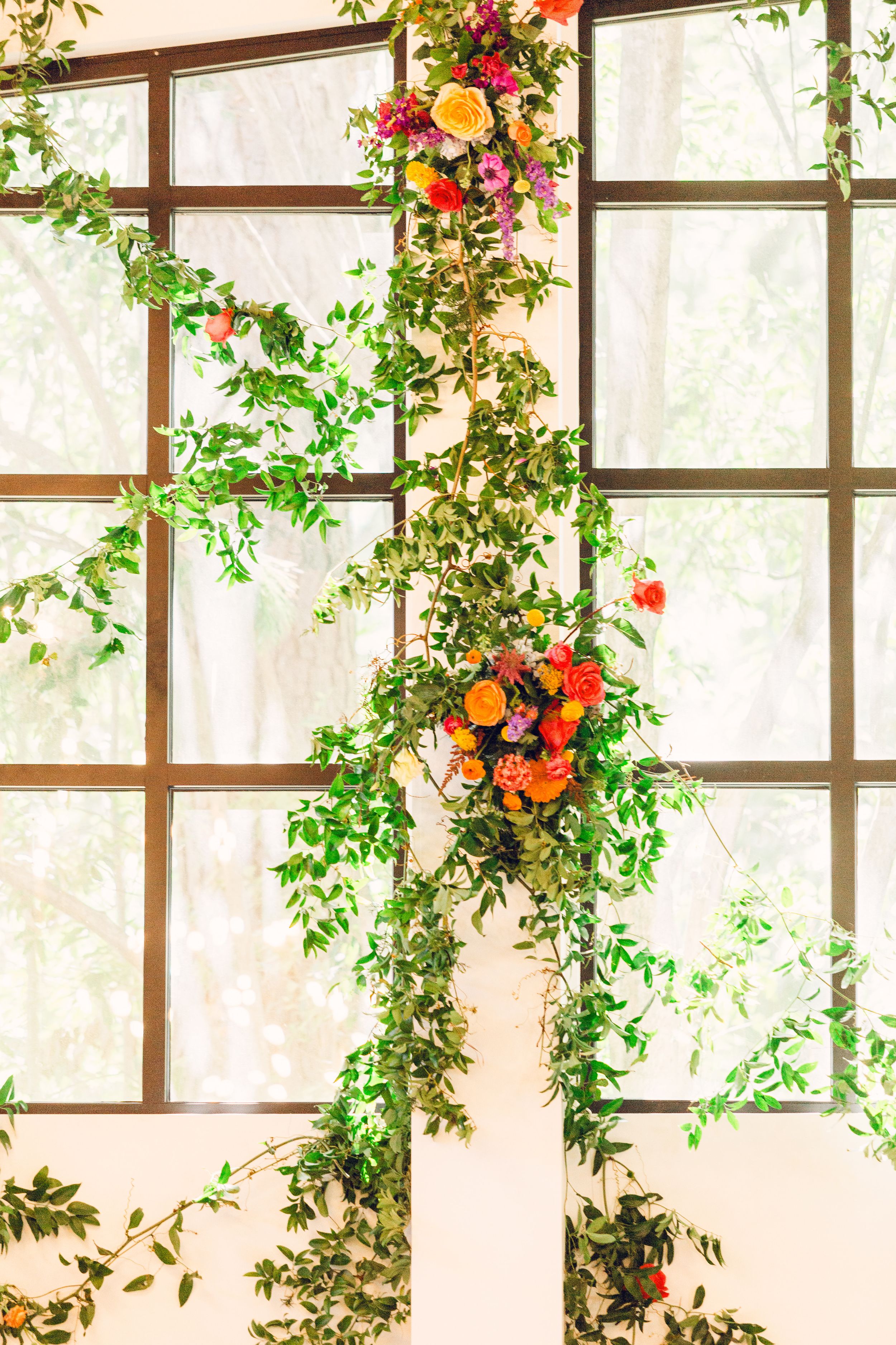 Colorful floral arrangements with orange and red blooms cascade down white lattice panels in an elegant indoor setting.