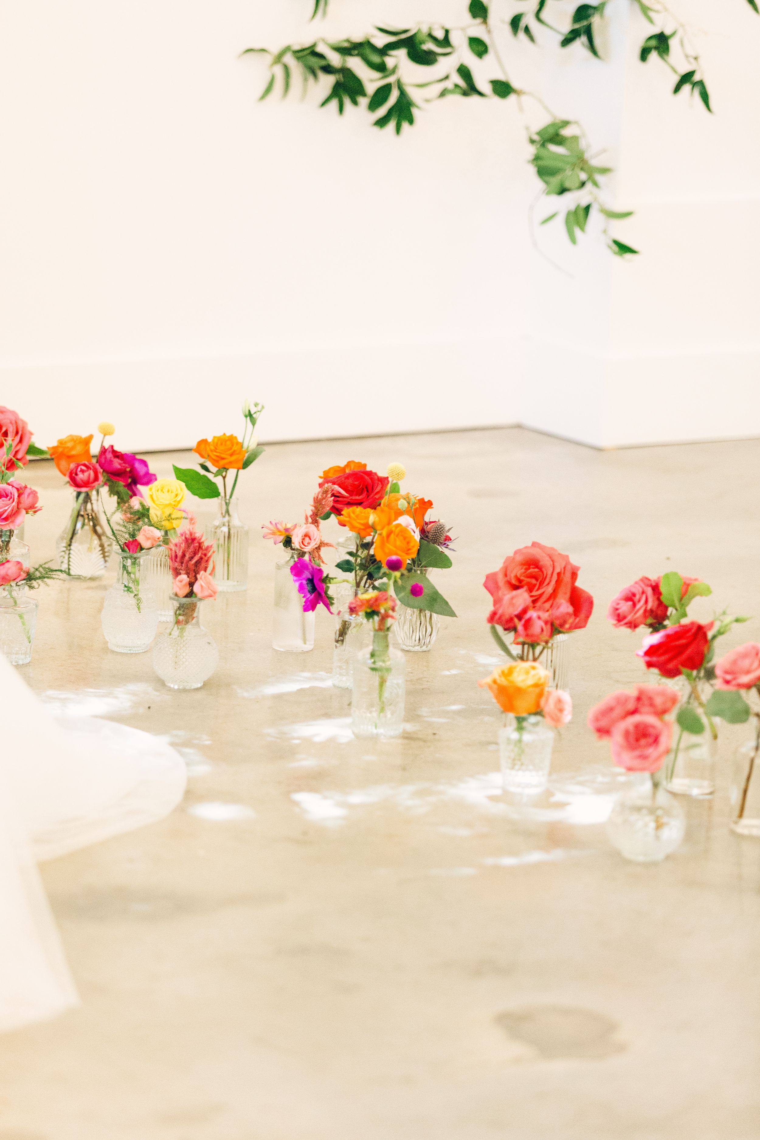 Simple wedding table decor features small glass vases filled with vibrant coral and orange flowers on a white tablecloth.