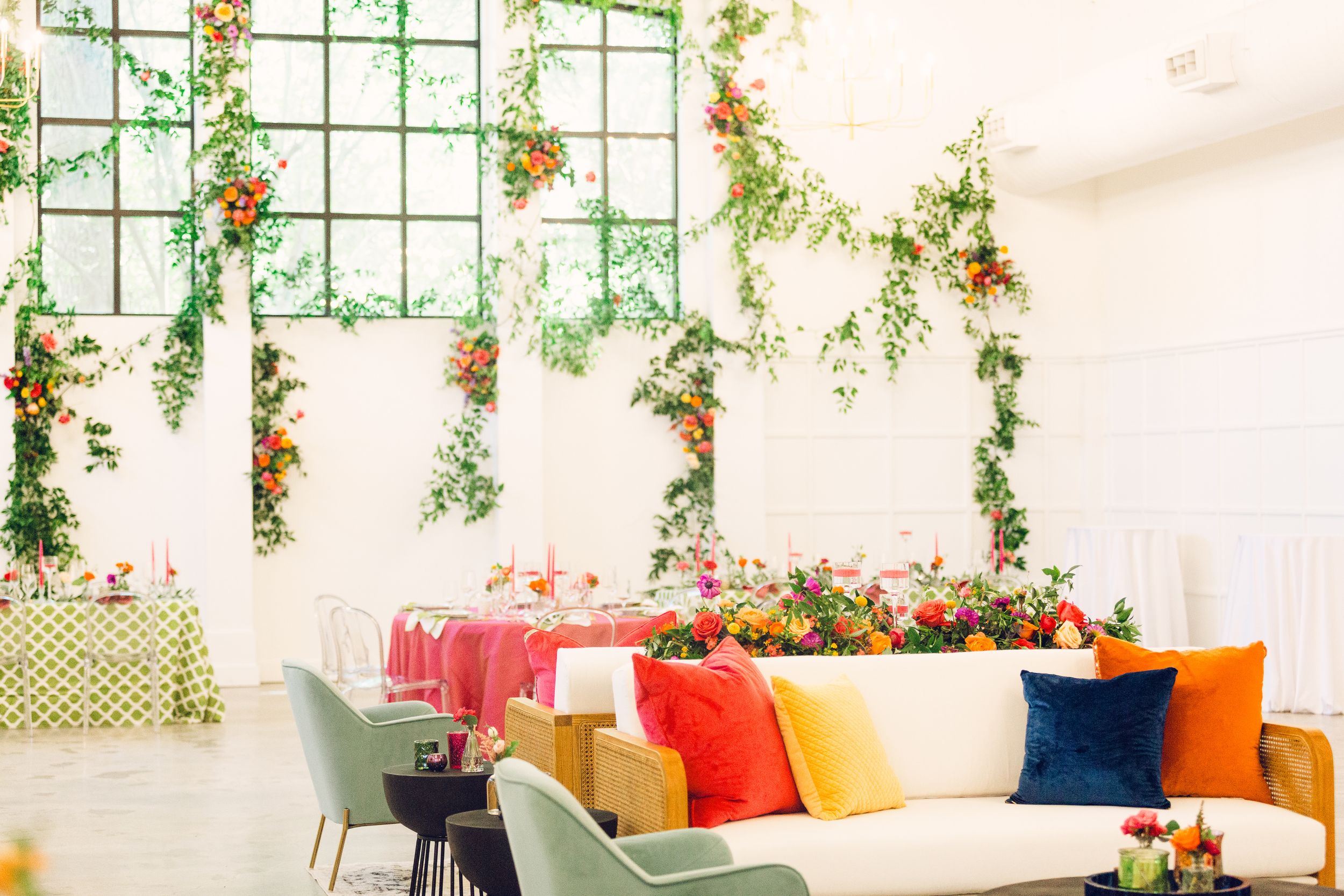Indoor wedding venue decorated with hanging greenery and colorful accent pillows.