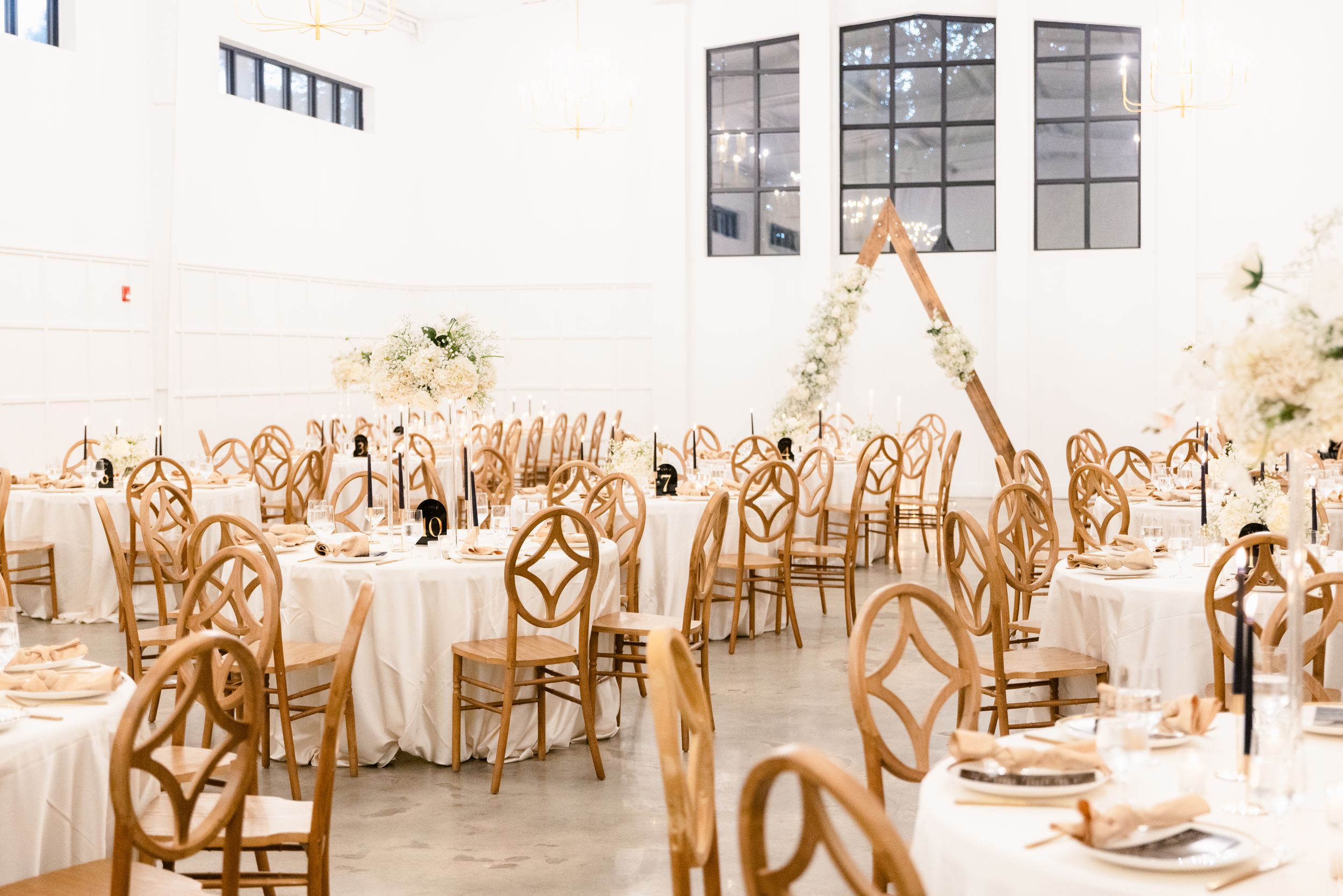 Wedding reception tables decorated in white and gold with elegant place settings and floral centerpieces in a bright venue.