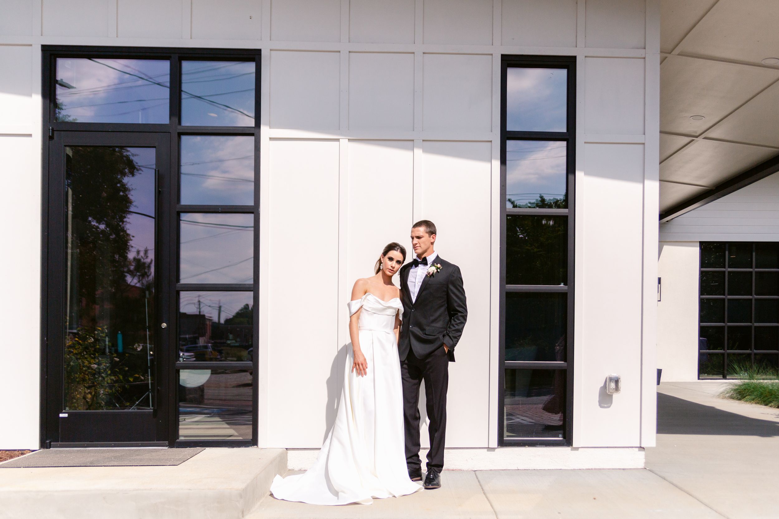A wedding couple poses for romantic photos in front of a modern white building at sunset.
