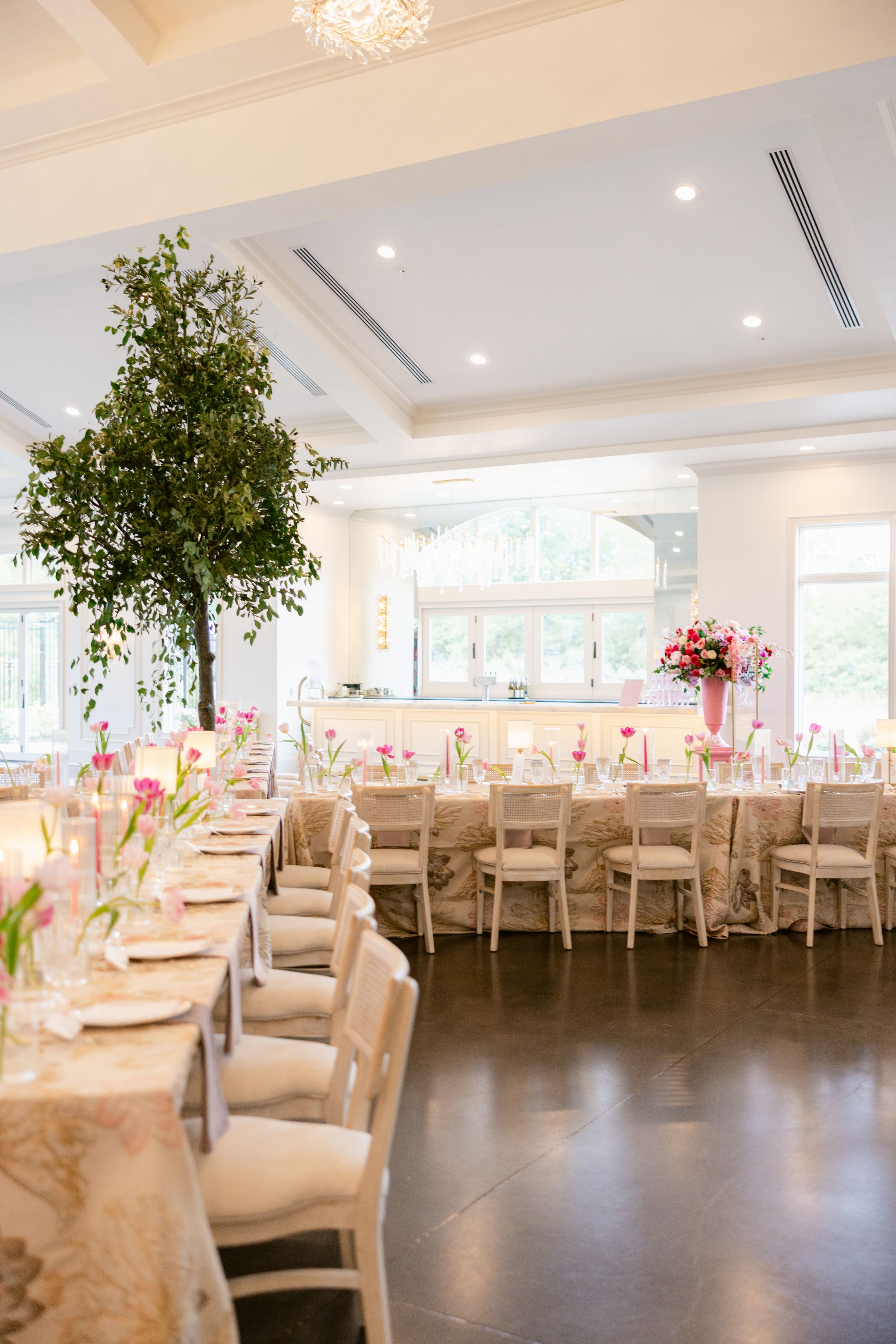 Elegant wedding reception venue with cream chair covers, tall centerpieces, and recessed lighting in a modern ballroom setting.