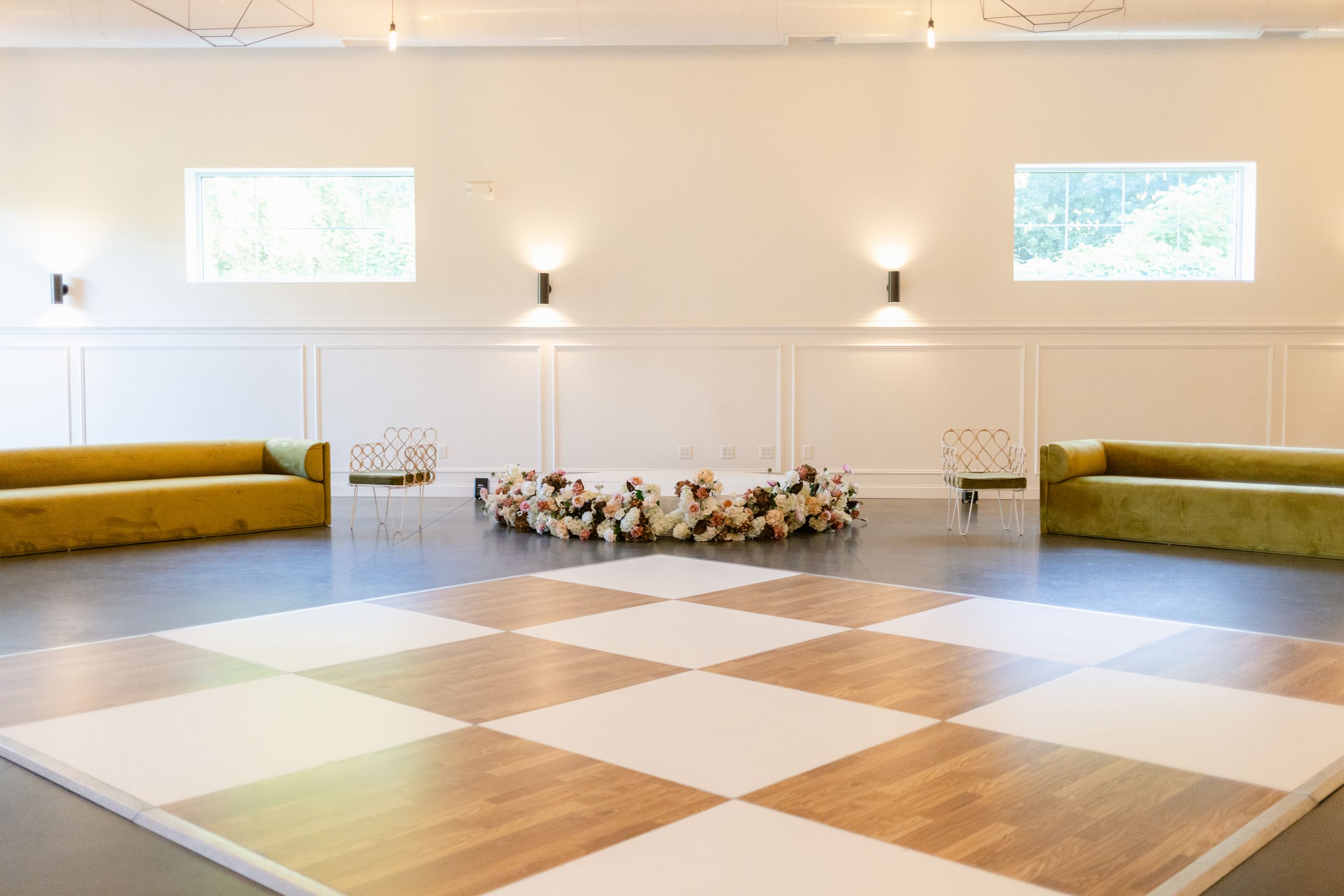 Large empty dance studio with checkered wood flooring and mirrored walls illuminated by natural light.