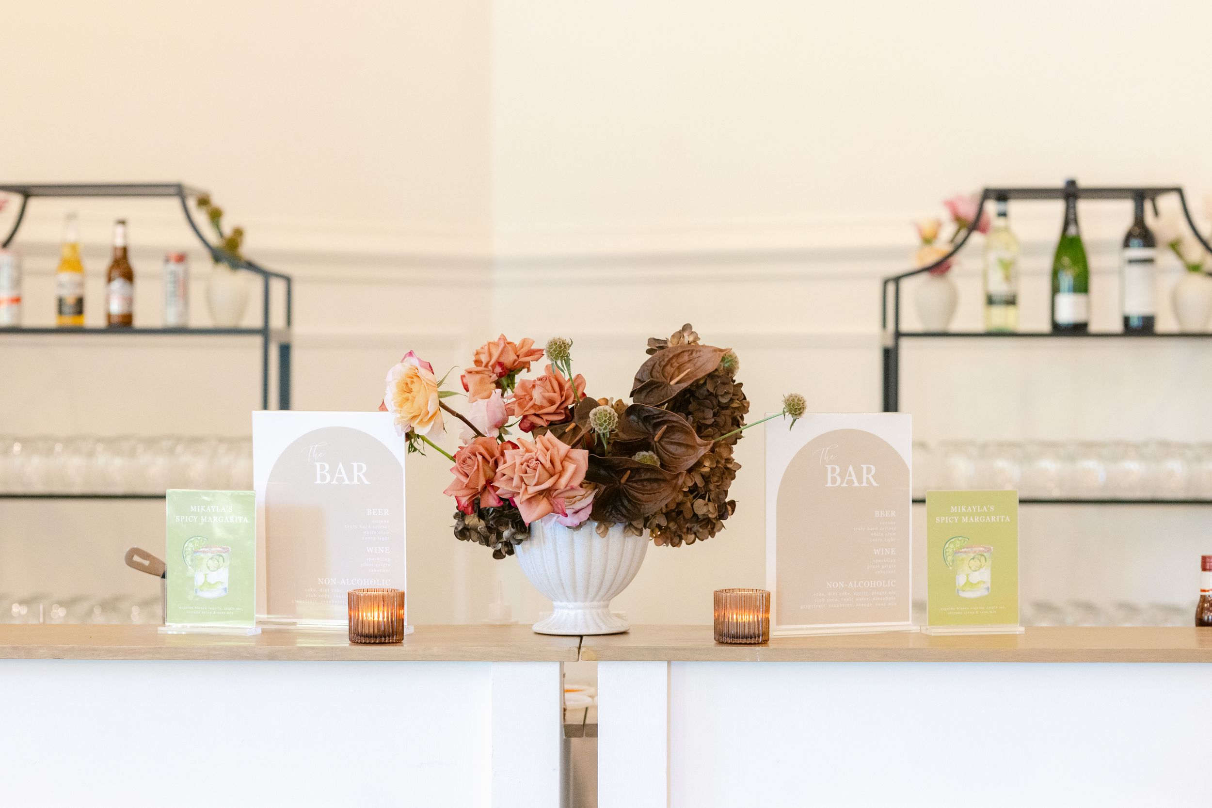 A soft pink and white event space decorated with elegant floral arrangements and candles on wooden tables.