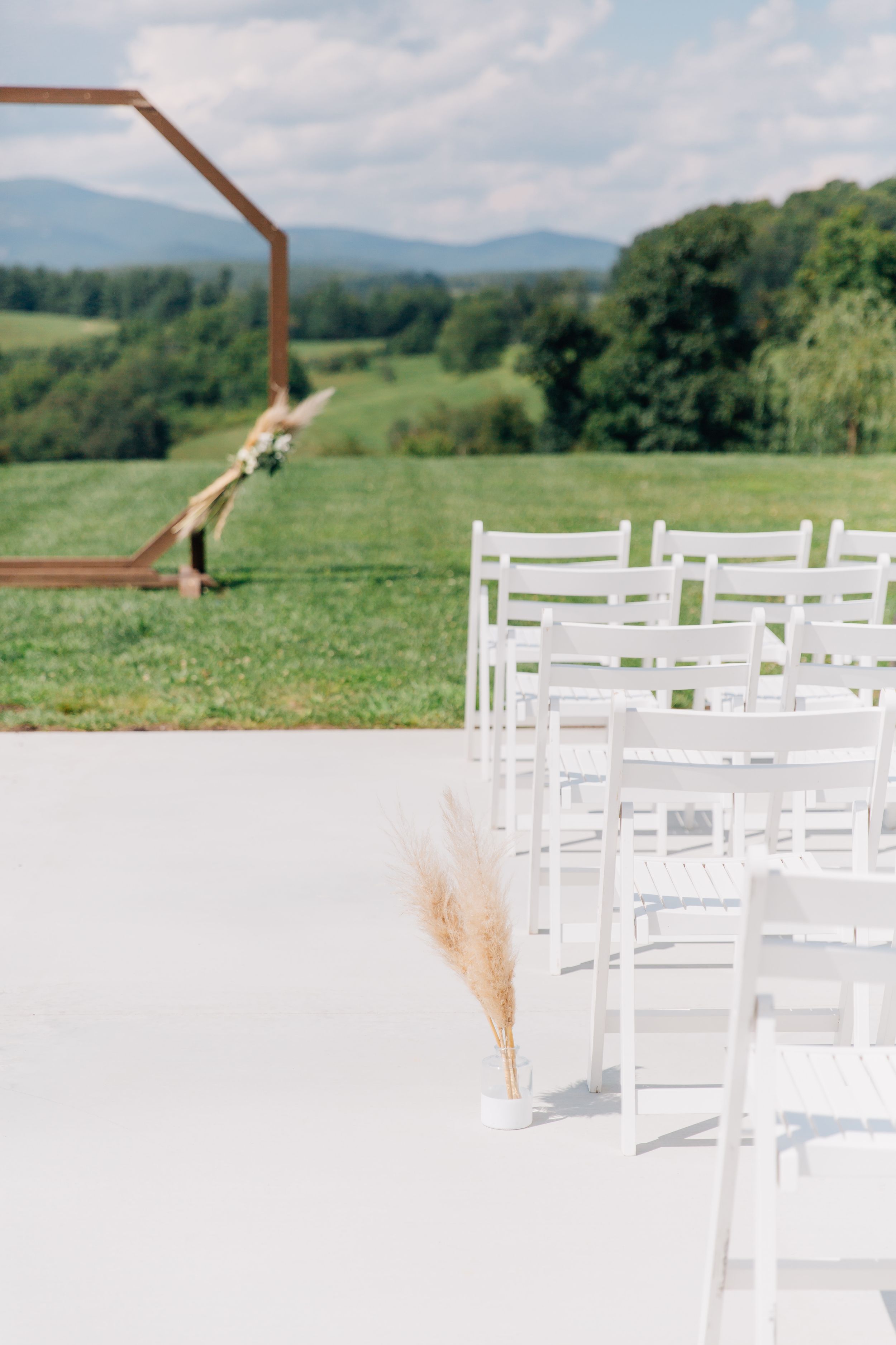 White wooden chairs arranged outdoors for a wedding ceremony with mountain views and natural pampas grass decor.