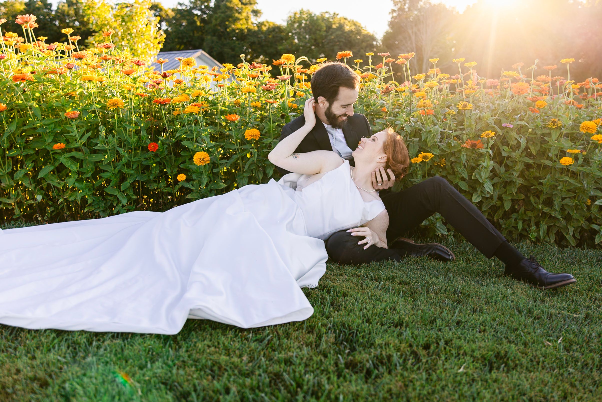 A figure in white dress lies gracefully on grass surrounded by vibrant yellow flowers at golden hour.