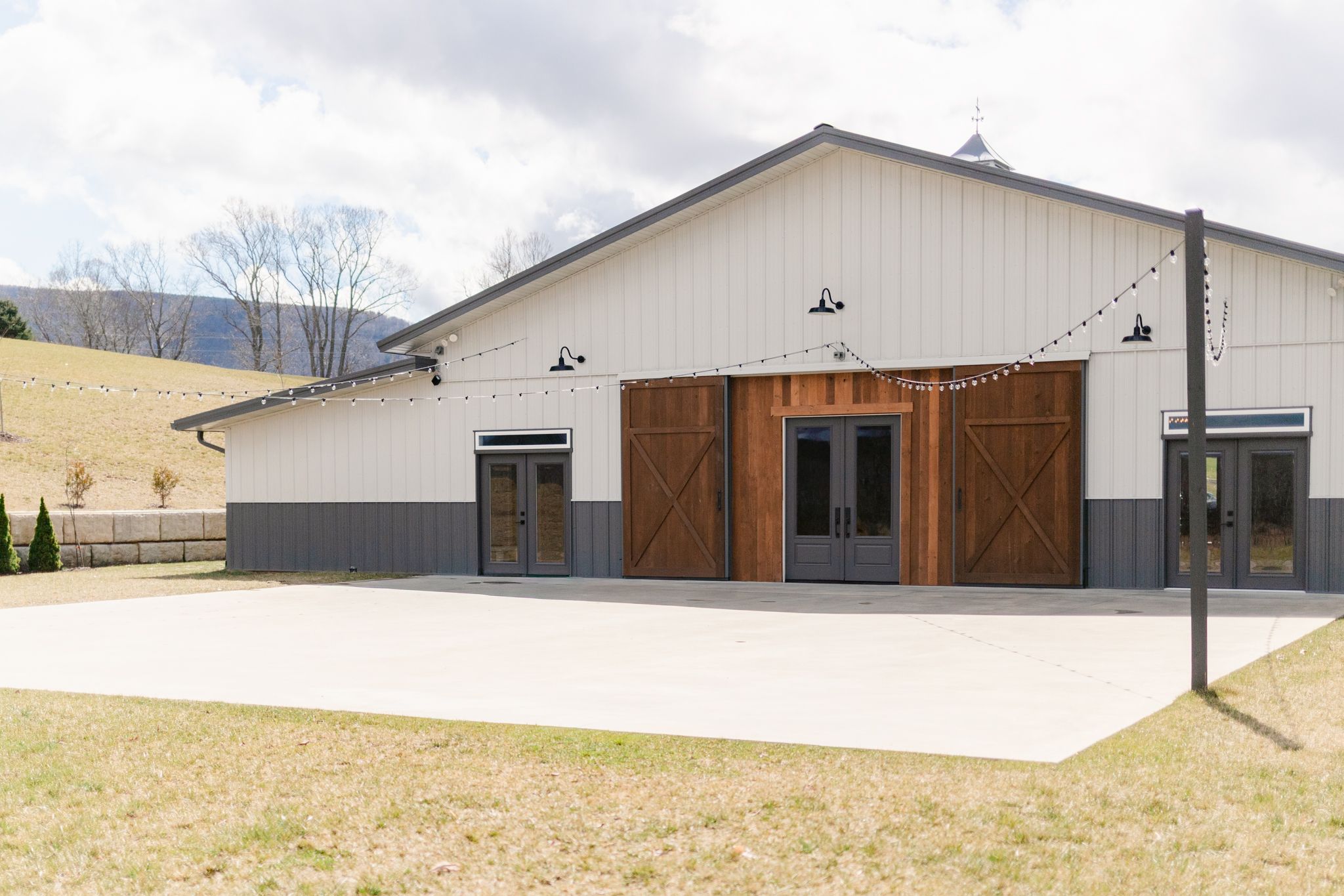 Modern white barn-style wedding venue with rustic wooden doors and metal accents set against rolling countryside.
